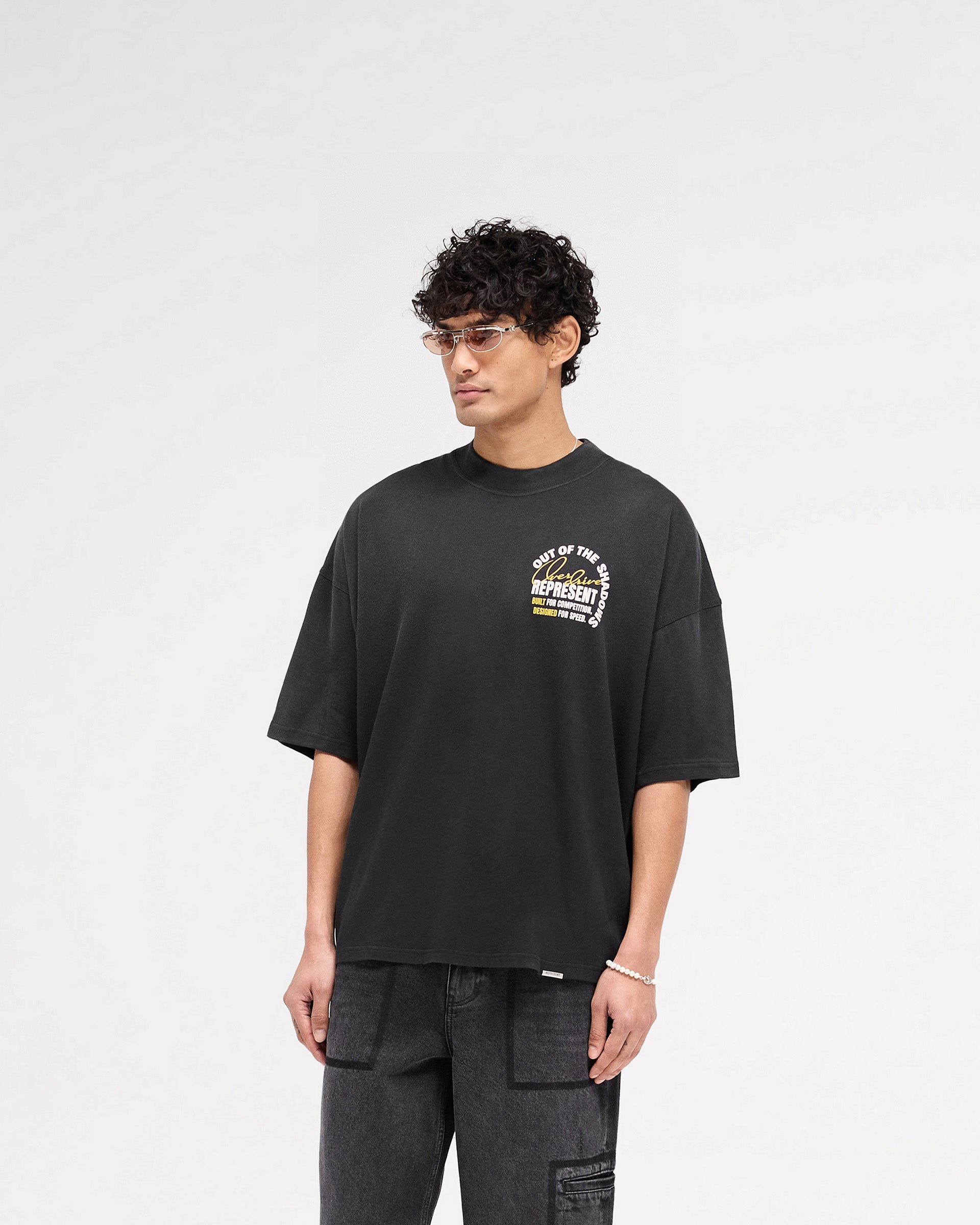 Man wearing a black graphic t-shirt on a plain white background | Out Of The Shadows T-Shirt in Stained Black | Boxy fit with a fade out wash | SS25 T-Shirts | Represent Clo