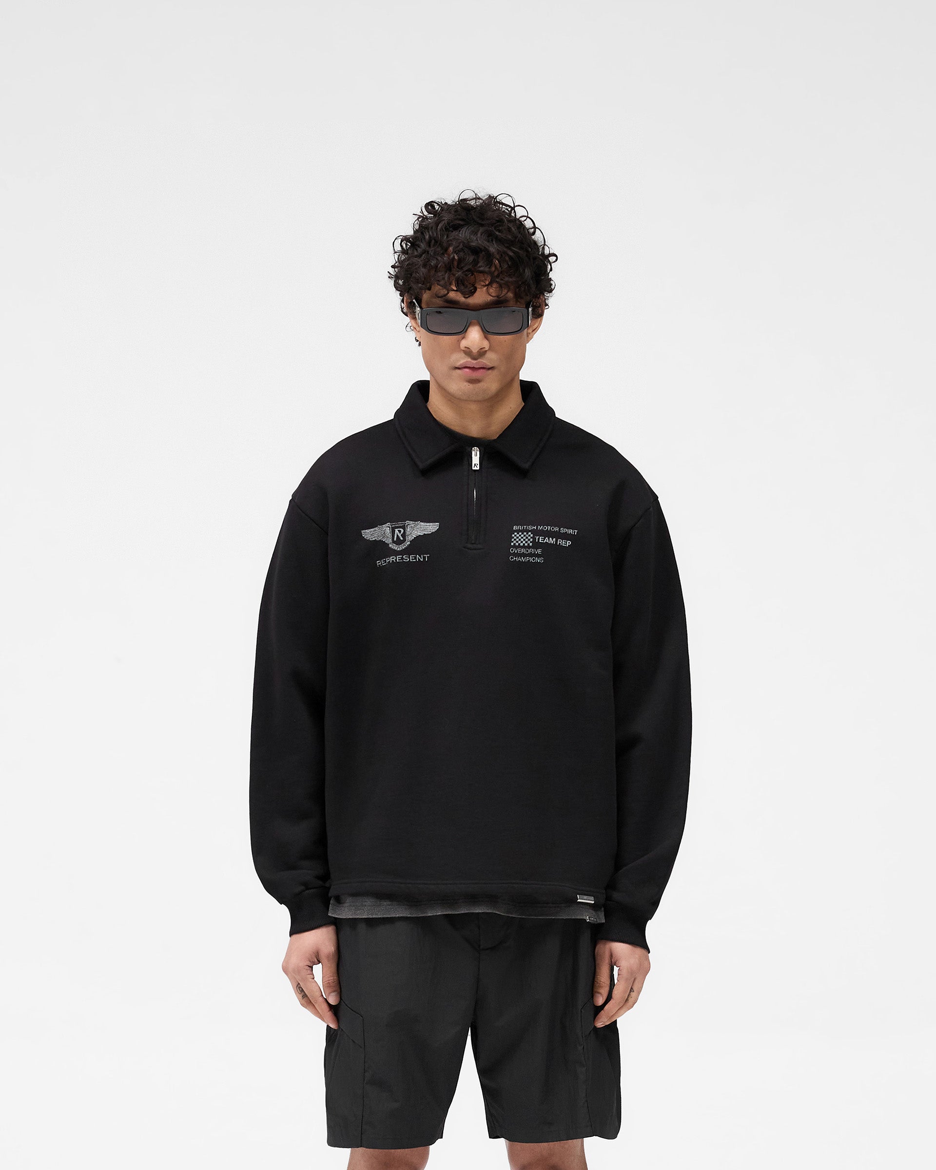 Man wearing an oversized black sweater on a plain white background | Team Rep Quarter Zip in Jet Black | Oversized sweater with vintage graphic and quarter zip | SS25 Sweaters | Represent Clo