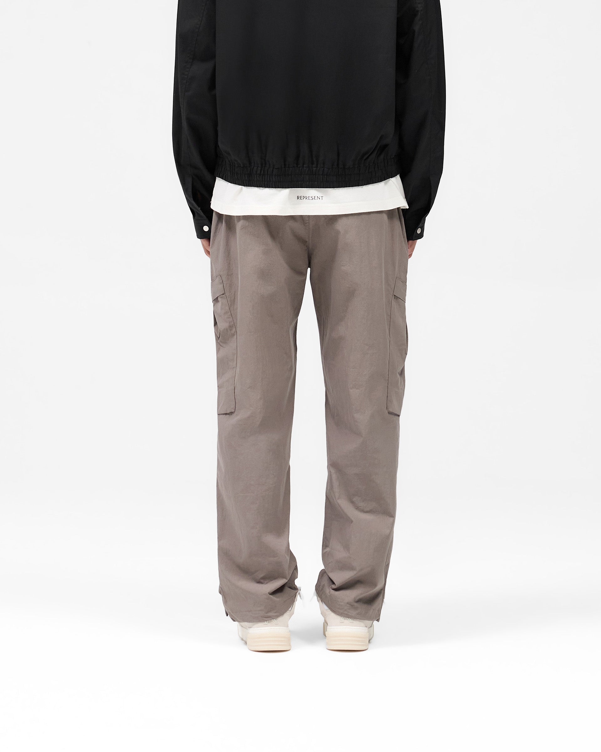 Man wearing mid grey cargo pants on a plain white background | Tech Cargo Pant in Mid Grey | Cargo pants with pleated pockets and adjustable hem | SS25 Pants | Represent Clo