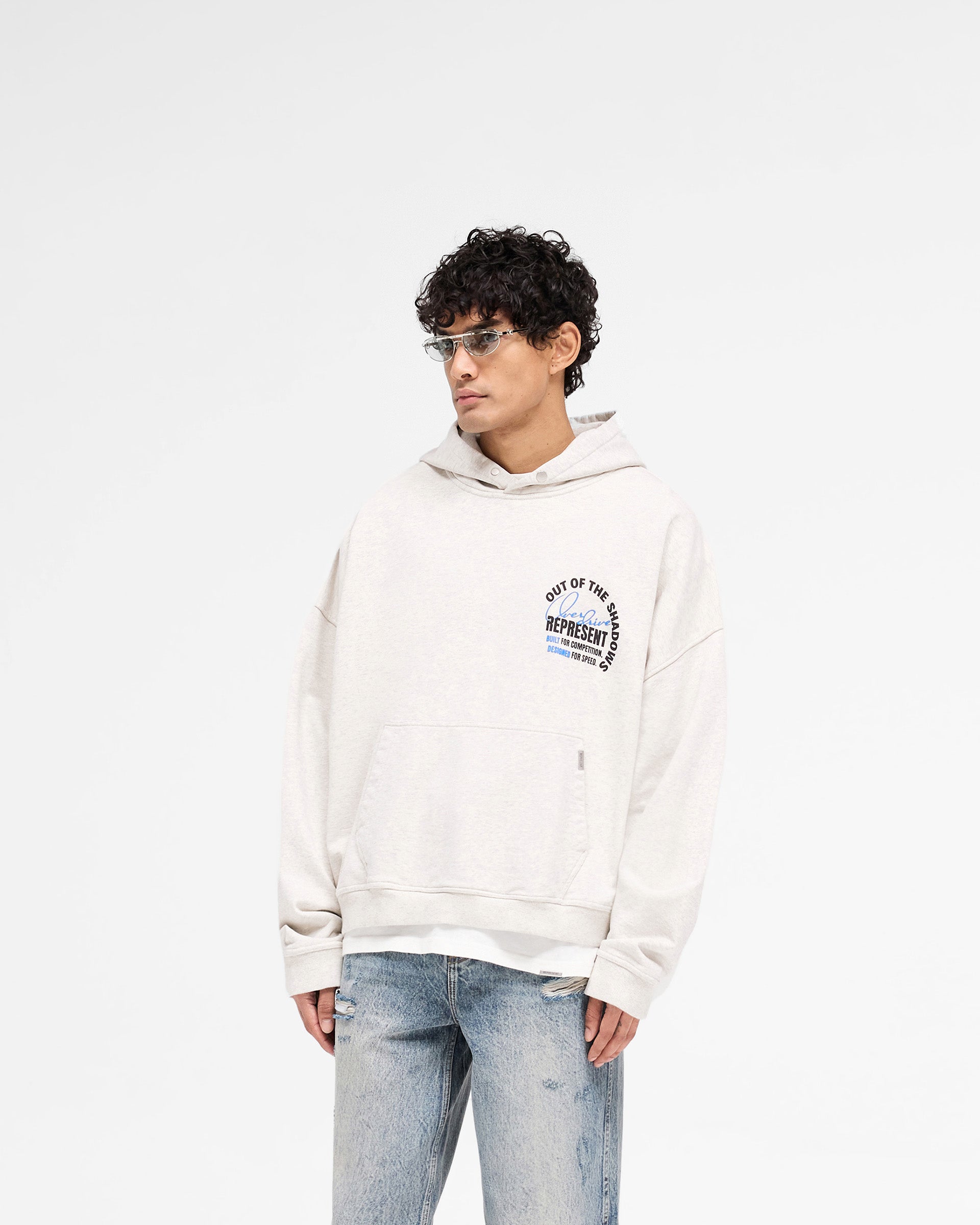 Man wearing an oversized cream hoodie on a plain white background | Out Of The Shadows Hoodie in Cream Marl | Boxy fit hoodie with Cobrax popper fastening | SS25 Hoodies | Represent Clo