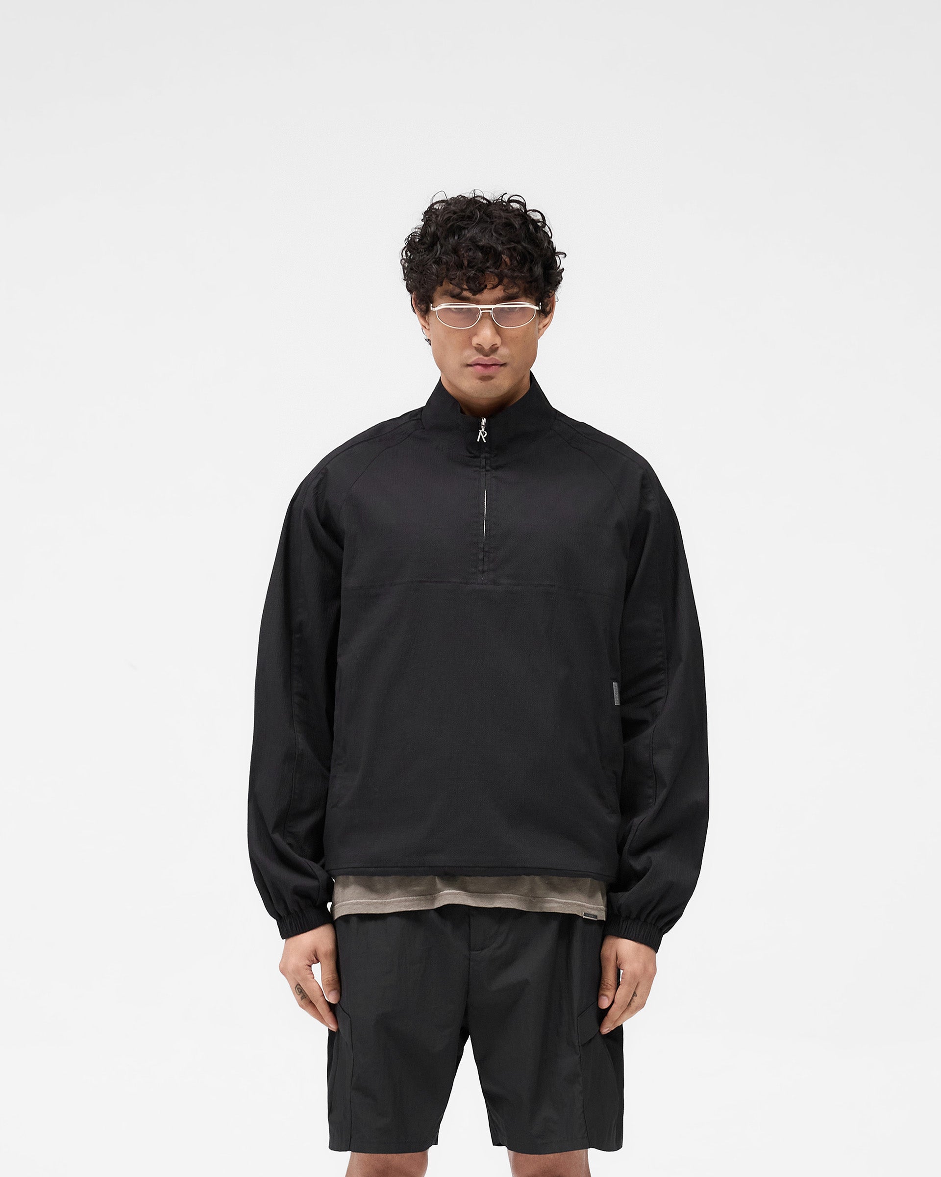 Man wearing a black quarter zip jacket on a plain white background | Quarter Zip Jacket in Black | Lightweight oversized outerwear with elasticated cuffs | SS25 Outerwear | Represent Clo
