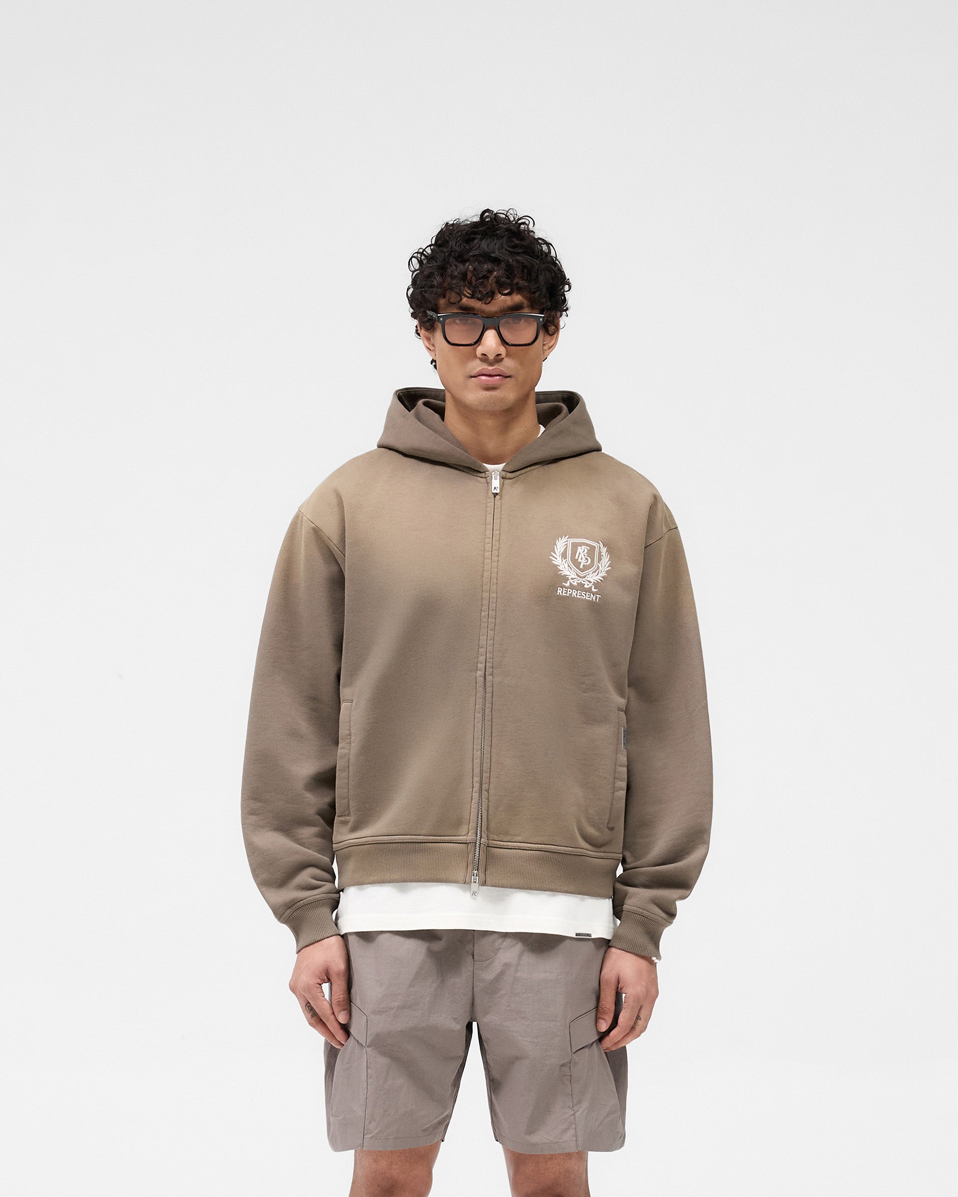 Man wearing an oversized taupe hoodie on a plain white background | Crest Zip Up Hoodie in Dark Taupe | Zip up hoodie with metal zip heads | SS25 Hoodies | Represent Clo