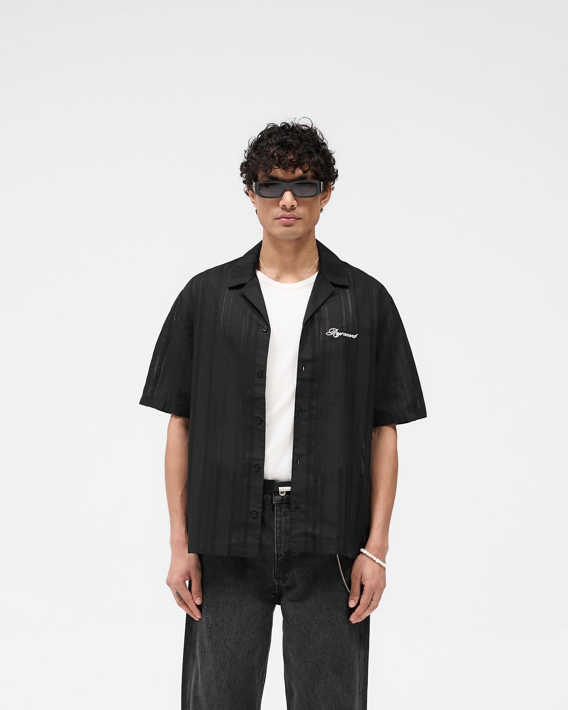 Man wearing a black bowling shirt on a plain white background | Embroidered Bowling Shirt in Jet Black | Sheer fabric shirt with embroidered logo | SS25 Shirts | Represent Clo