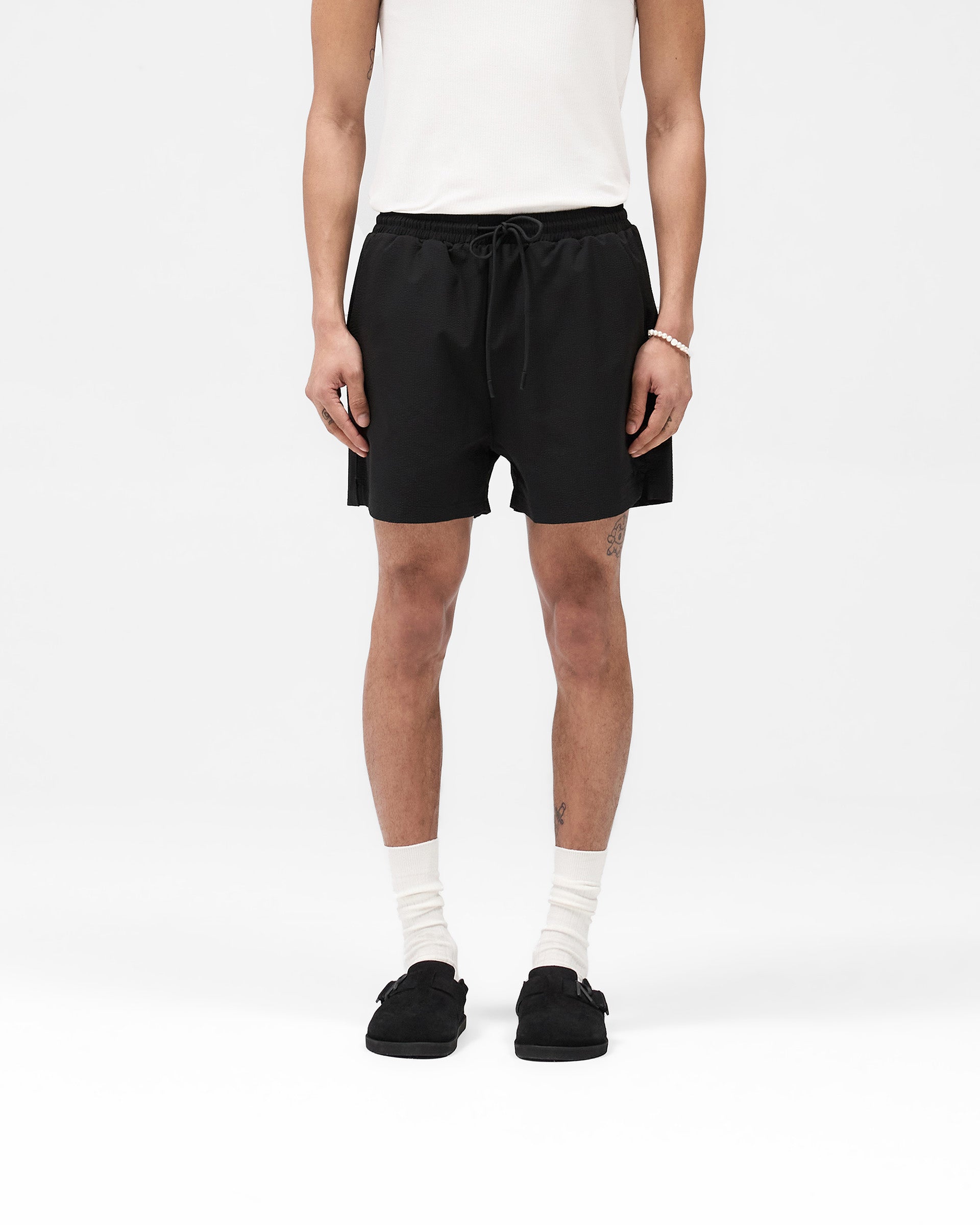 Man wearing a black swim short on a plain white background | Seersucker Smart Swim Short in Black | Swim shorts with internal lining and embroidered logo | SS25 Shorts | Represent Clo