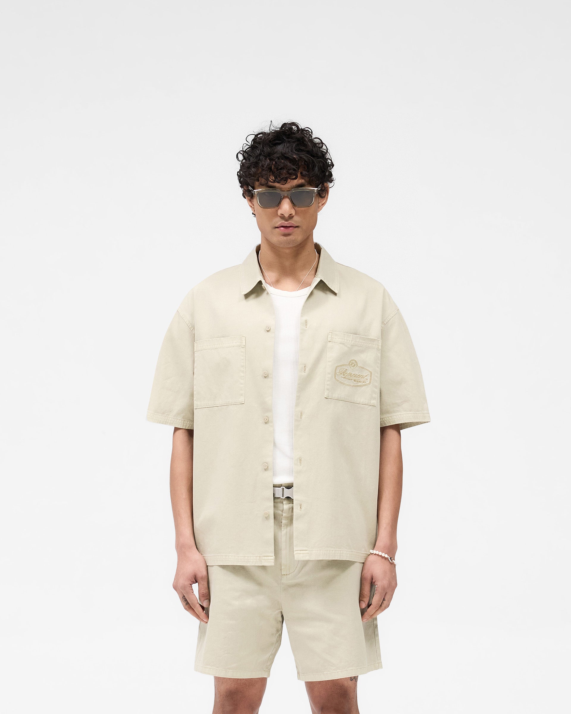Man wearing a beige short sleeve overshirt on a plain white background | Short Sleeve Cotton Overshirt in Beige | Rigid twill with dual chest pockets | SS25 Shirts | Represent Clo