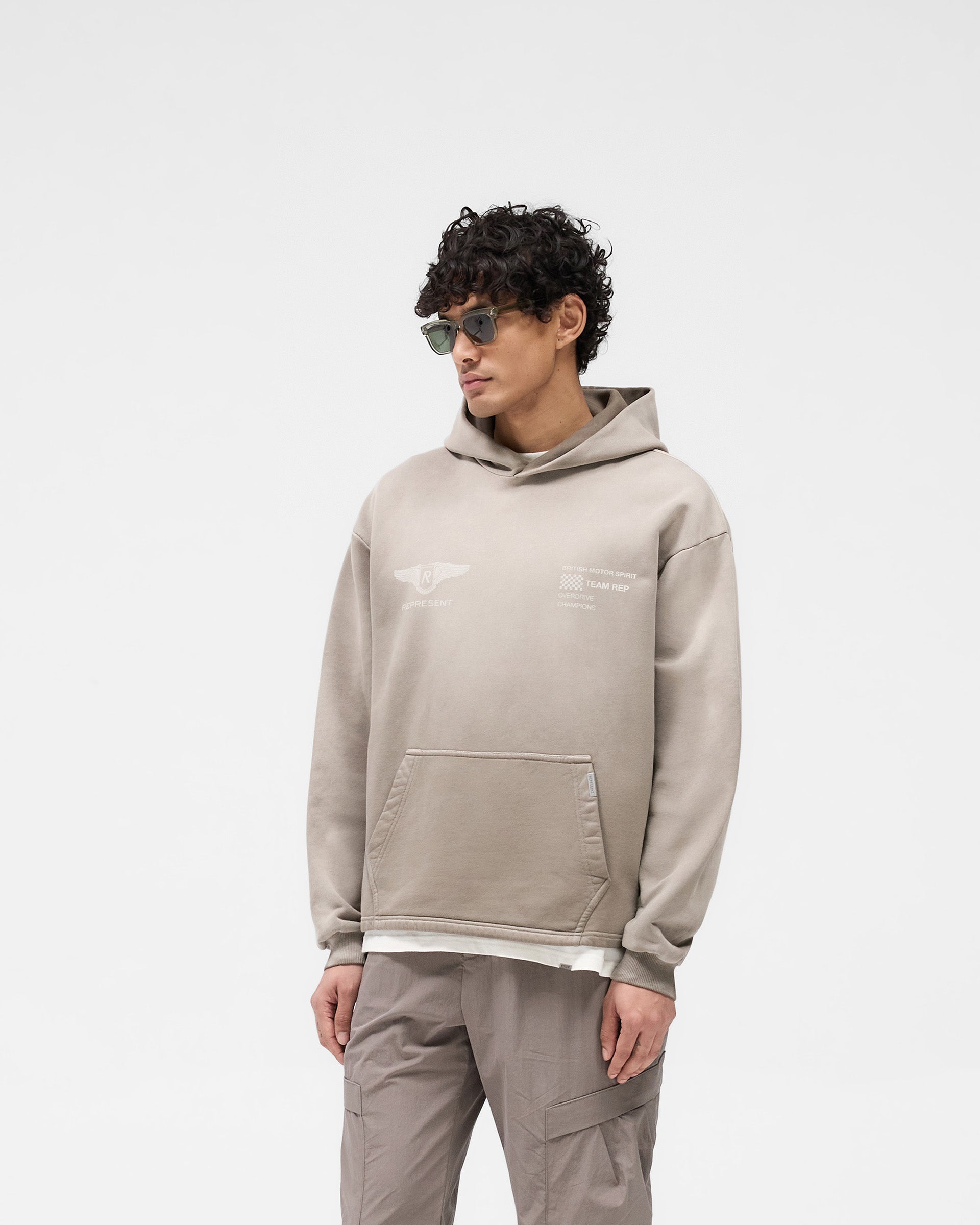 Man wearing an oversized dark taupe hoodie on a plain white background | Team Rep Hoodie in Dark Taupe | Oversized hoodie with vintage graphic | SS25 Hoodies | Represent Clo