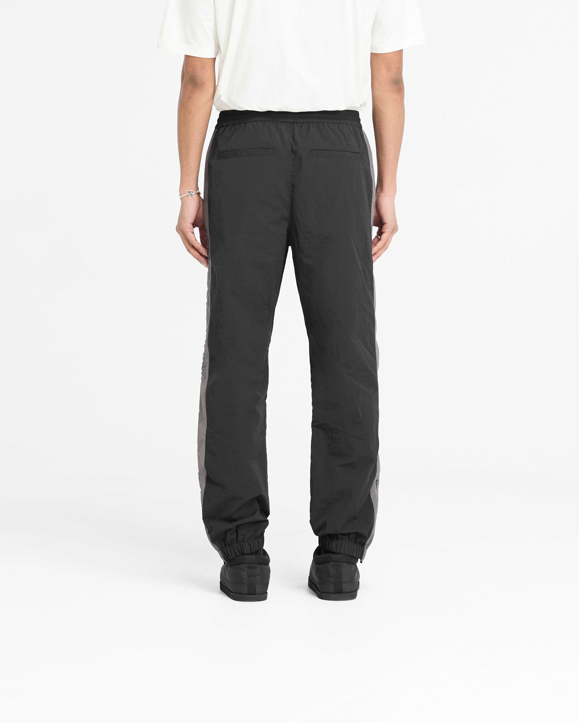Man wearing black nylon track pants on a plain white background | Nylon Track Pant in Black | Track pants with elasticated cuff and hem zip | PRE SS25 Pants | Represent Clo