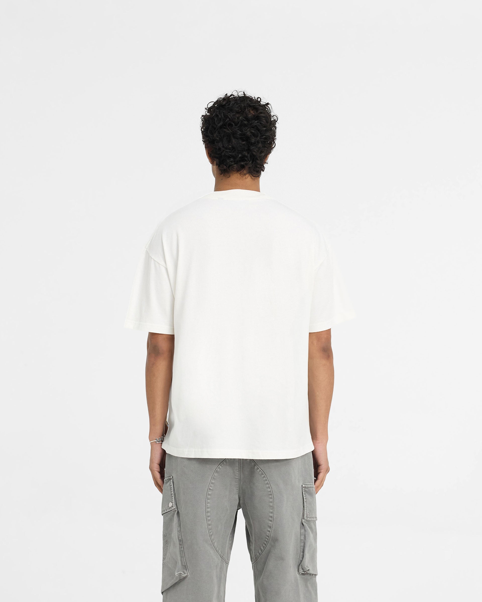 Man wearing a white t-shirt on a plain white background | Represent X Belstaff Patch T-Shirt in Flat White | Oversized t-shirt with woven patch branding | Exclusives T-Shirts | Represent Clo