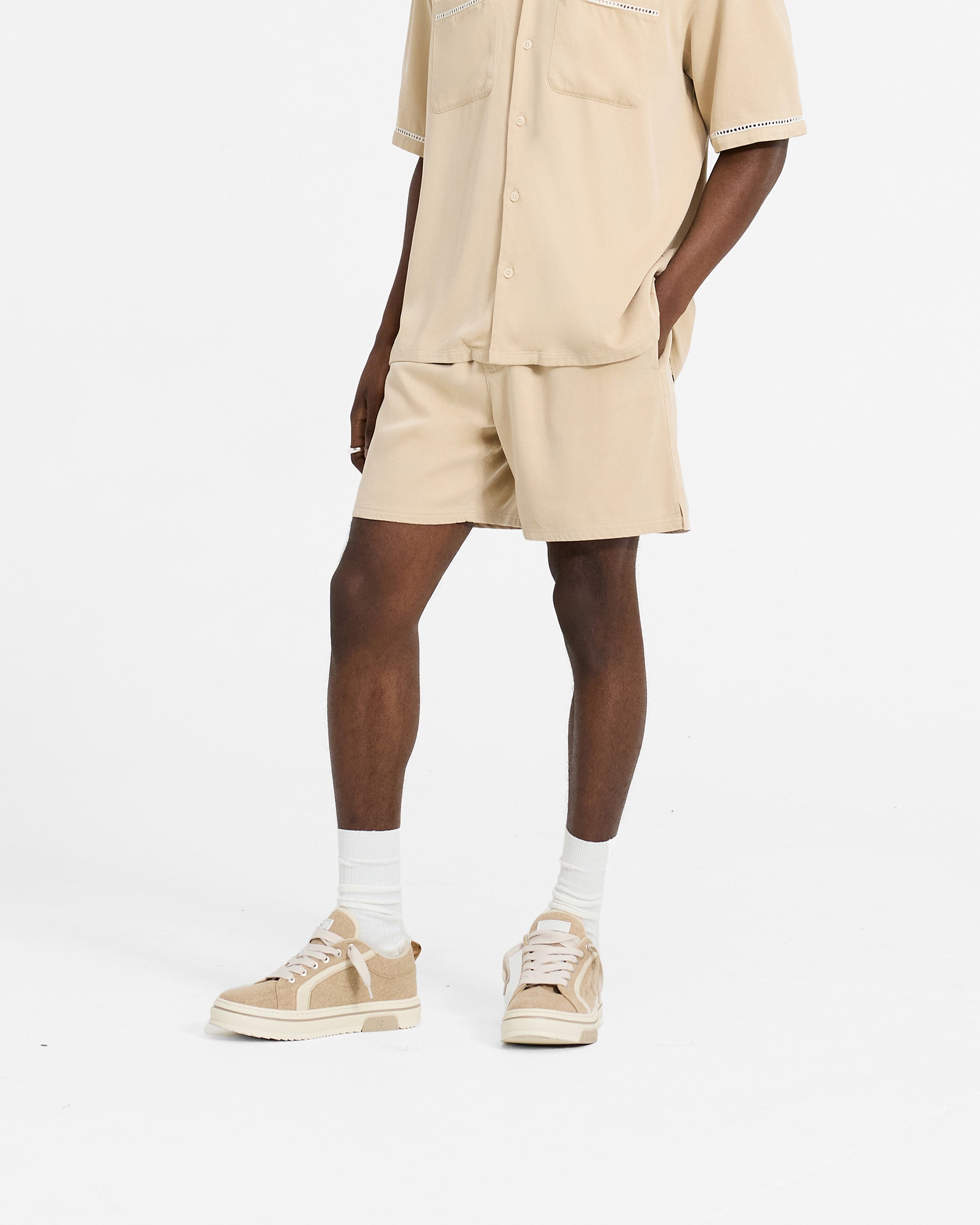 Man wearing relaxed fit mens brown shorts on a plain white background | Resort Shorts in Latte | Shorts with elasticated waistband and drawcord | SC24 Shorts | Represent Clo