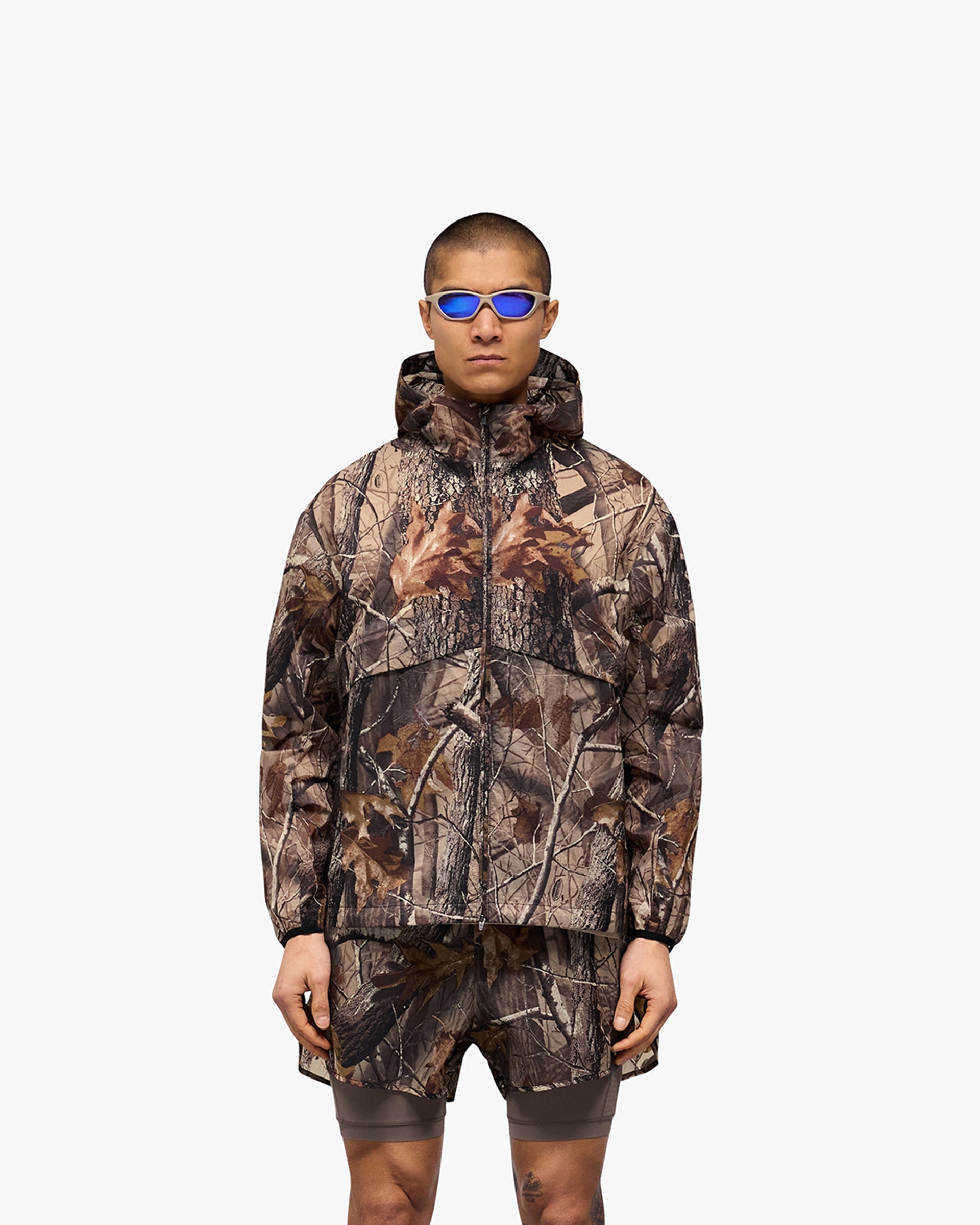 Man wearing a camouflage hooded jacket on a plain white background | 247 Hooded Training Jacket in Realtree | Polyester jacket with DWR coating and zip pockets | 247 Outerwear | Represent Clo