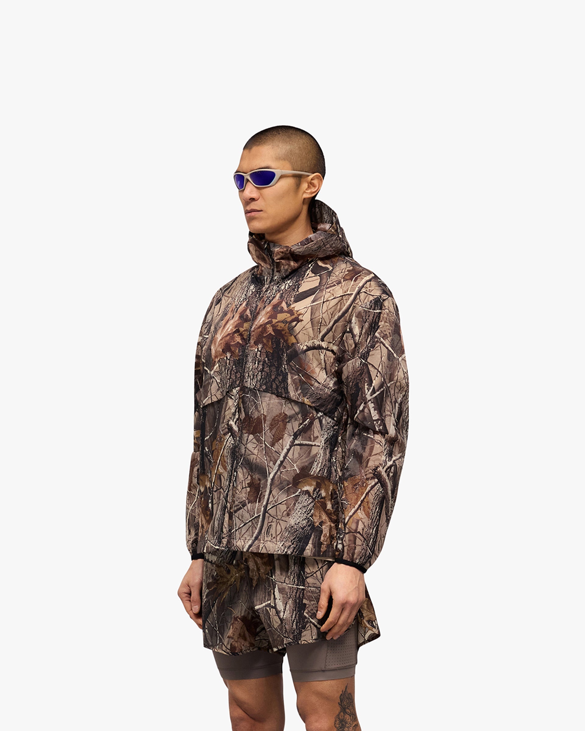 Man wearing a camo jacket on a plain white background | 247 Hooded Training Jacket in Realtree | Performance jacket with DWR coating and adjustable toggles | 247 Outerwear | Represent Clo
