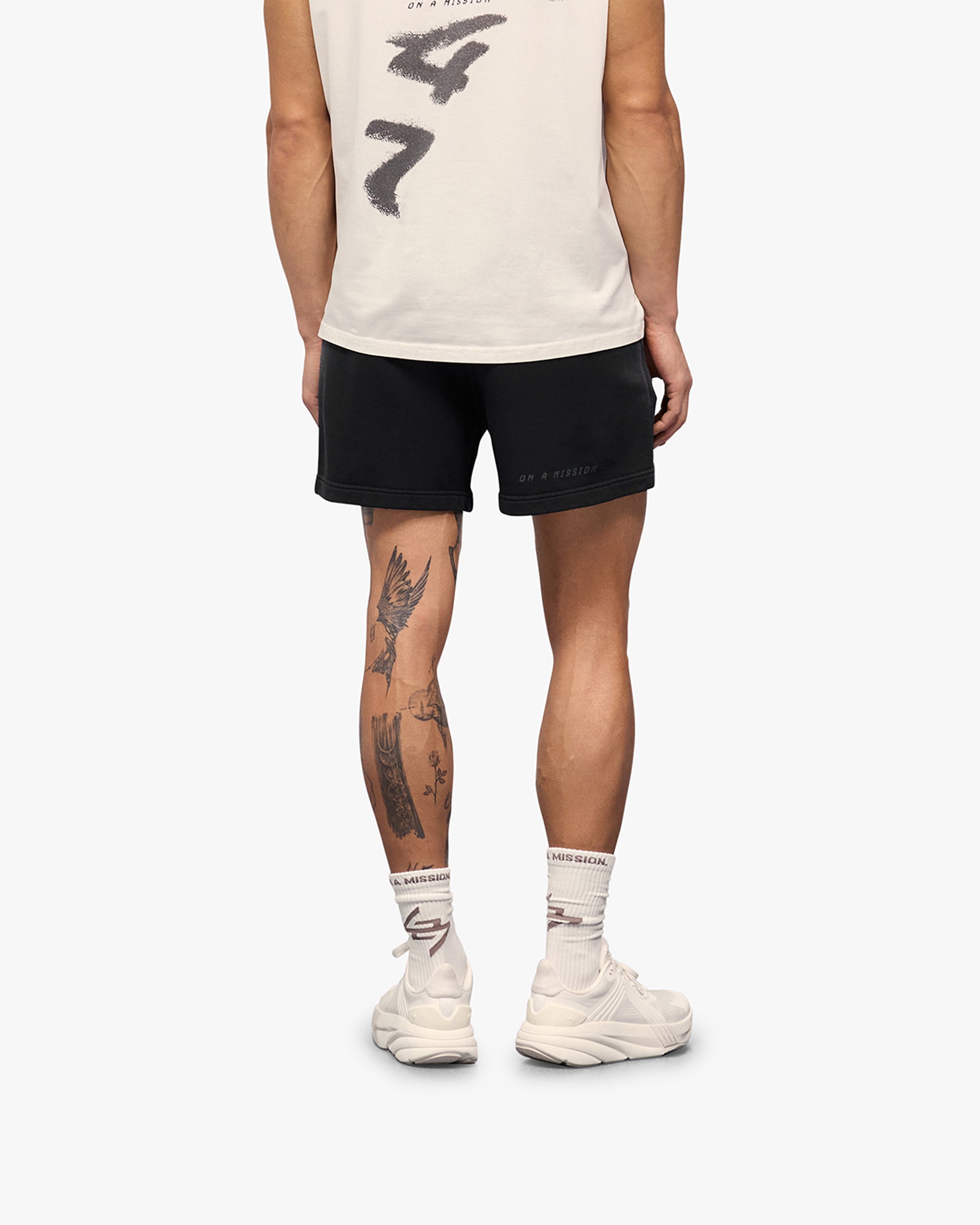 Man wearing aged black shorts on a plain white background | 247 Motion Shorts in Aged Black | Shorts with elasticated waistband and graphic print | 247 Shorts | Represent Clo