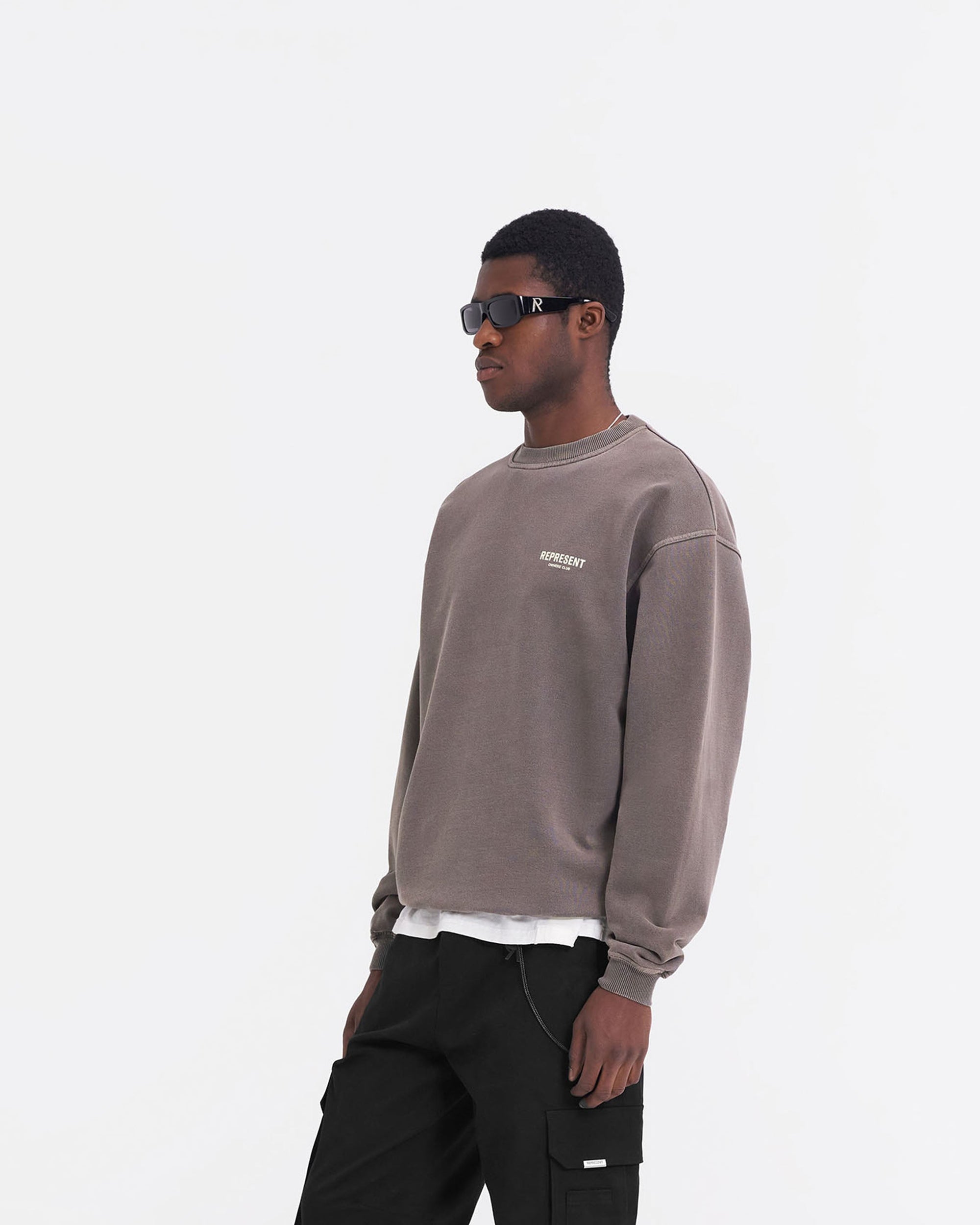 Man wearing an oversized grey sweater on a plain white background | Represent Owners Club Sweater in Fog | Oversized crewneck sweater with branding | Owners Club Sweaters | Represent Clo
