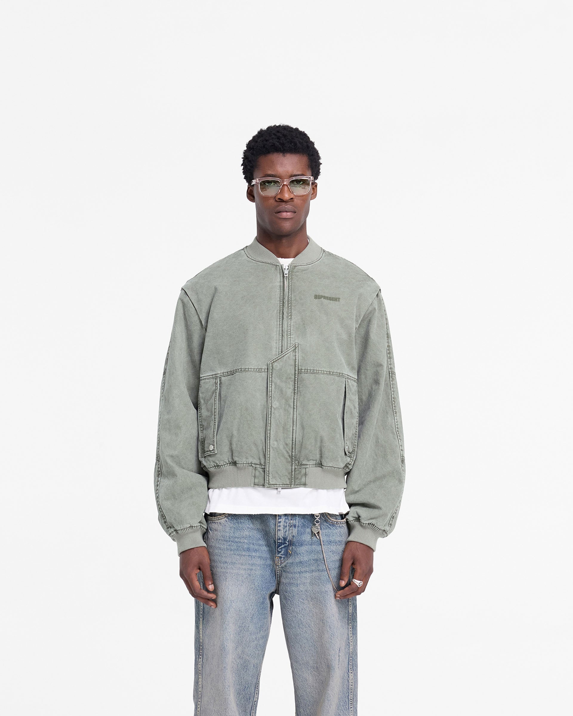 Man wearing a khaki bomber jacket on a plain white background | Inset Sleeve Bomber in Khaki | Cotton bomber jacket with asymmetric placket | FW24 Outerwear | Represent Clo