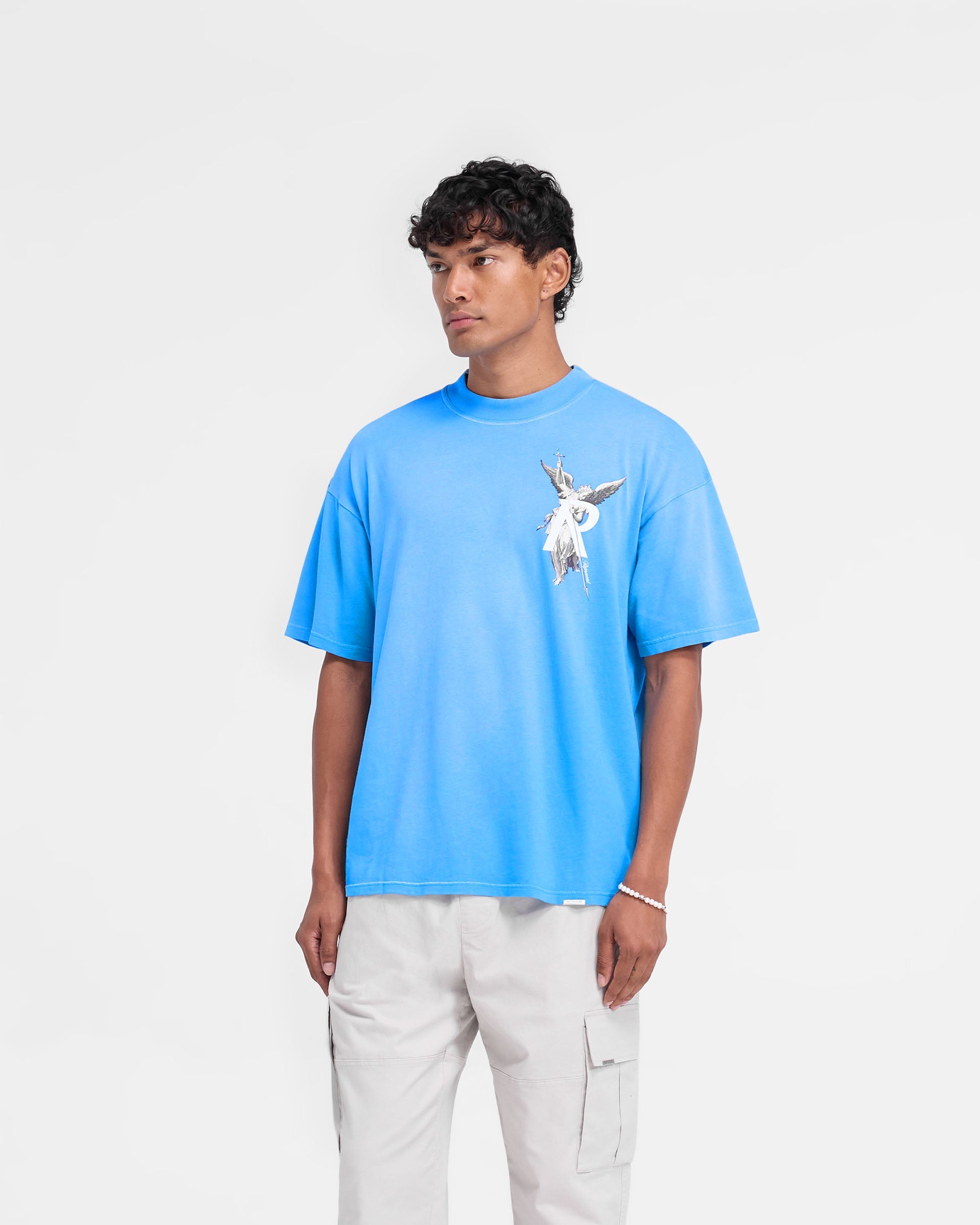 Man wearing a blue t-shirt on a plain white background | Archangel T-Shirt in Electric Blue | Slightly oversized t-shirt with high density graphic | FW24 T-Shirts | Represent Clo