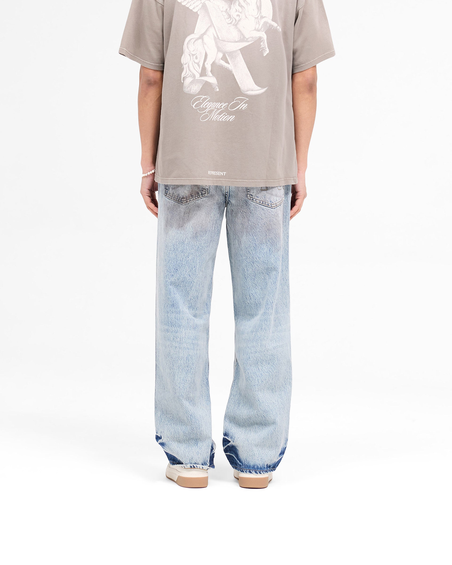Model wearing mens blue denim jeans on a plain white background | R3 Baggy Denim in Mechanic Blue | Baggy fit denim with patched dye and initial embroidery | SS25 Denim | Represent Clo