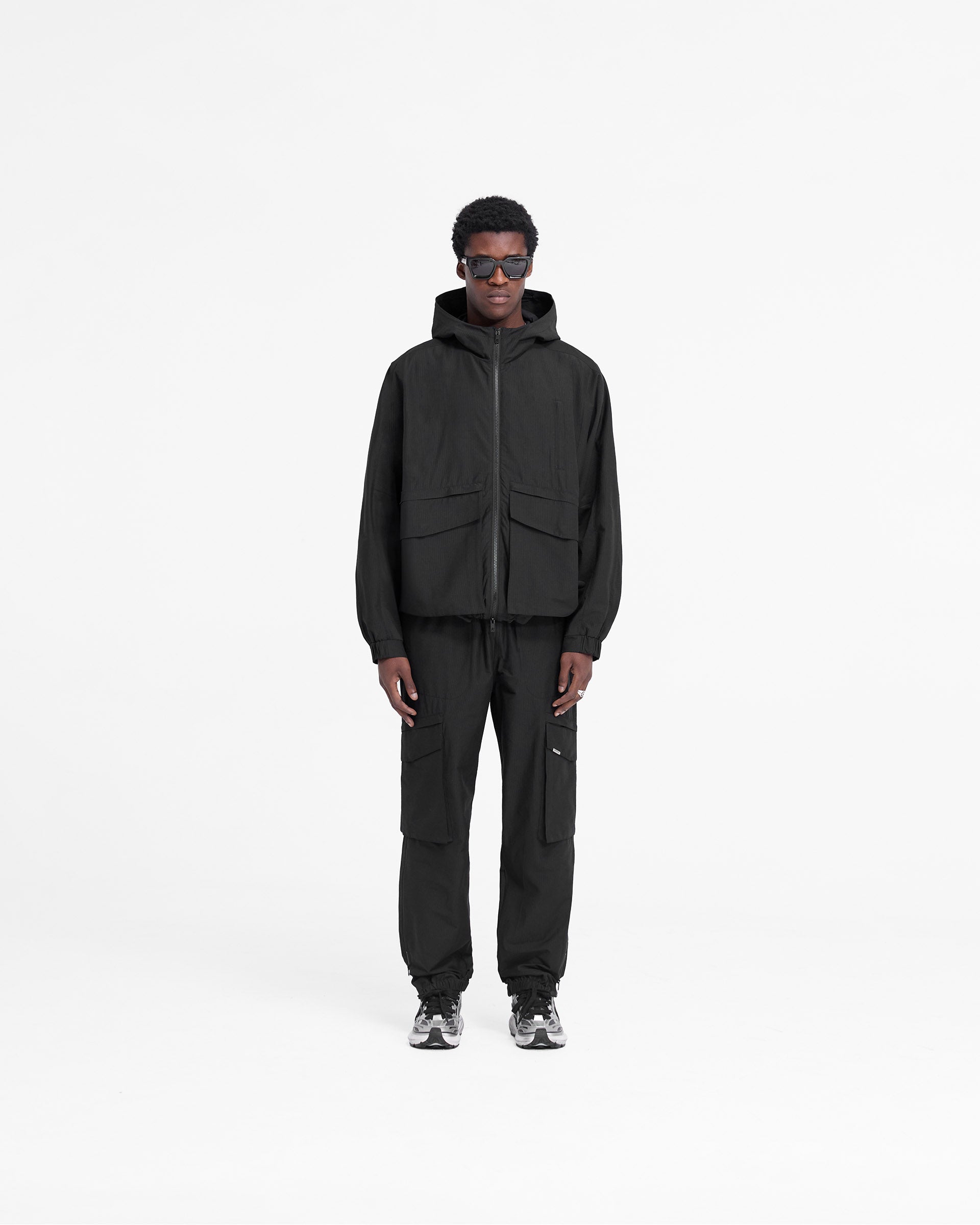 Man wearing a black jacket on a plain white background | Tech Cargo Jacket in Jet Black | Cotton blend jacket with oversized pockets | FW24 Outerwear | Represent Clo