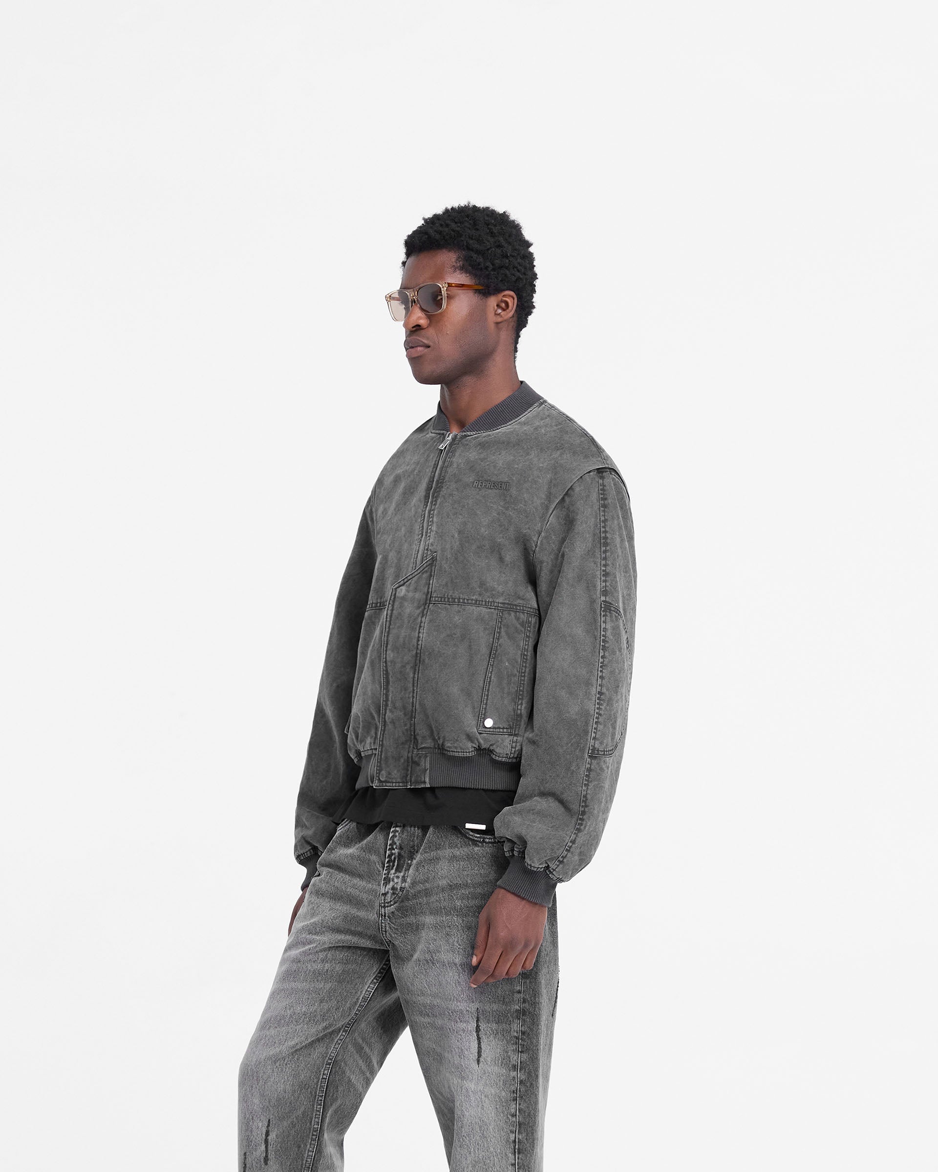 Man wearing a black bomber jacket on a plain white background | Inset Sleeve Bomber in Stained Black | Bomber jacket with asymmetric placket and zip guard | FW24 Outerwear | Represent Clo
