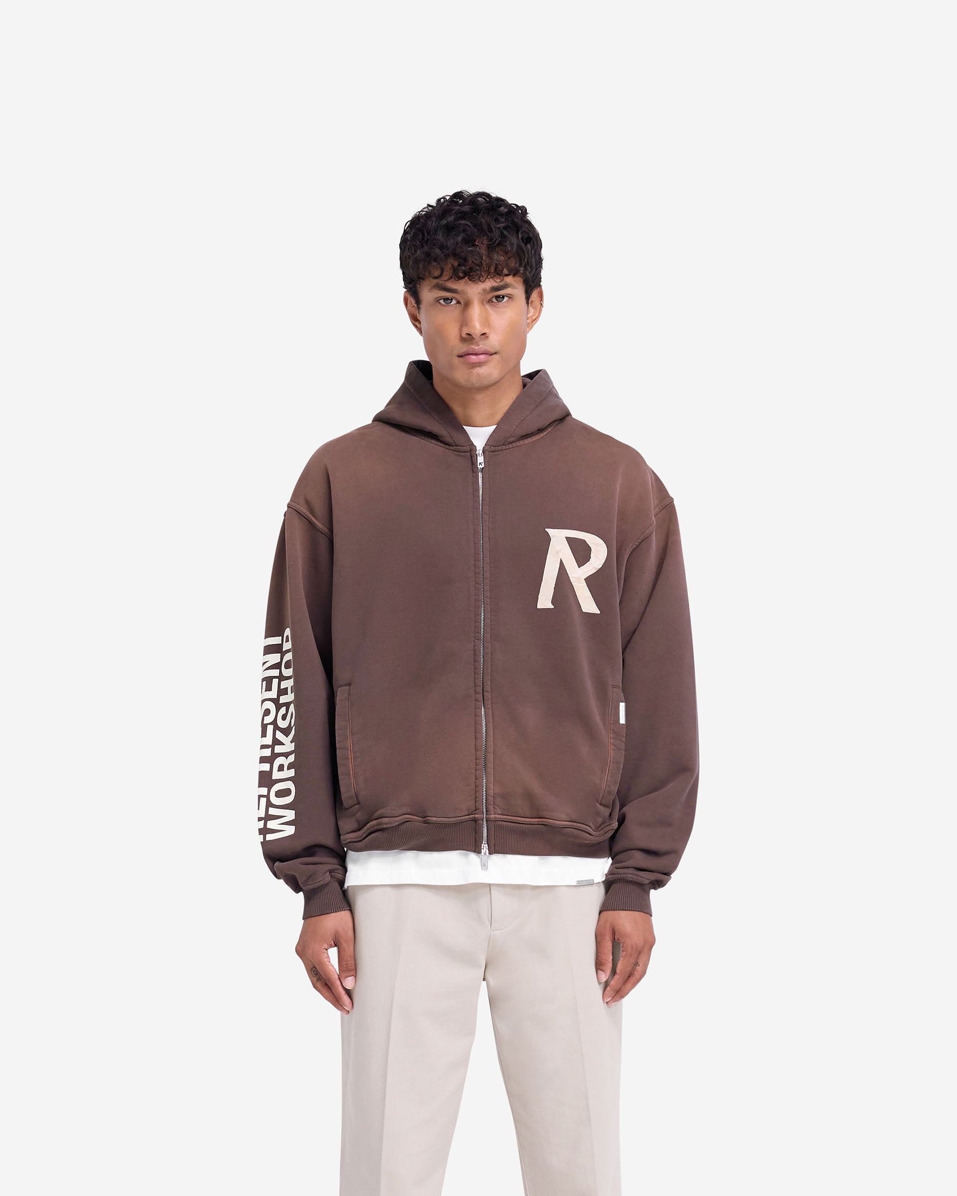 Man wearing a green zip hoodie on a plain white background | Masking Tape Initial Zip Hoodie in Cedar | Slightly oversized zip hoodie with cracked print sleeve | FW24 Hoodies | Represent Clo