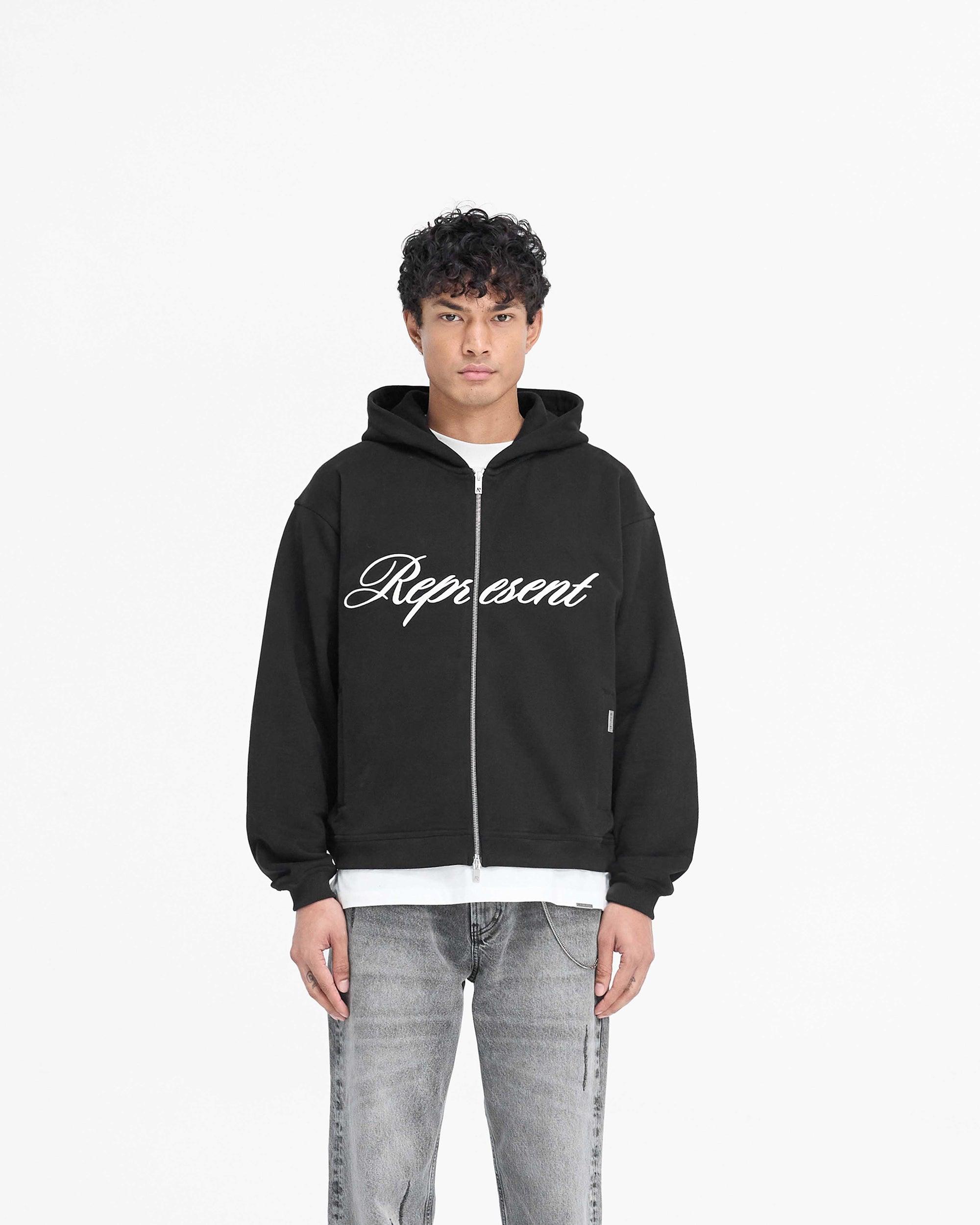 Man wearing a black zip hoodie on a plain white background | Script Logo Zip Hoodie in Black | Slightly oversized hoodie with RiRi double zip | PRE SS25 Hoodies | Represent Clo