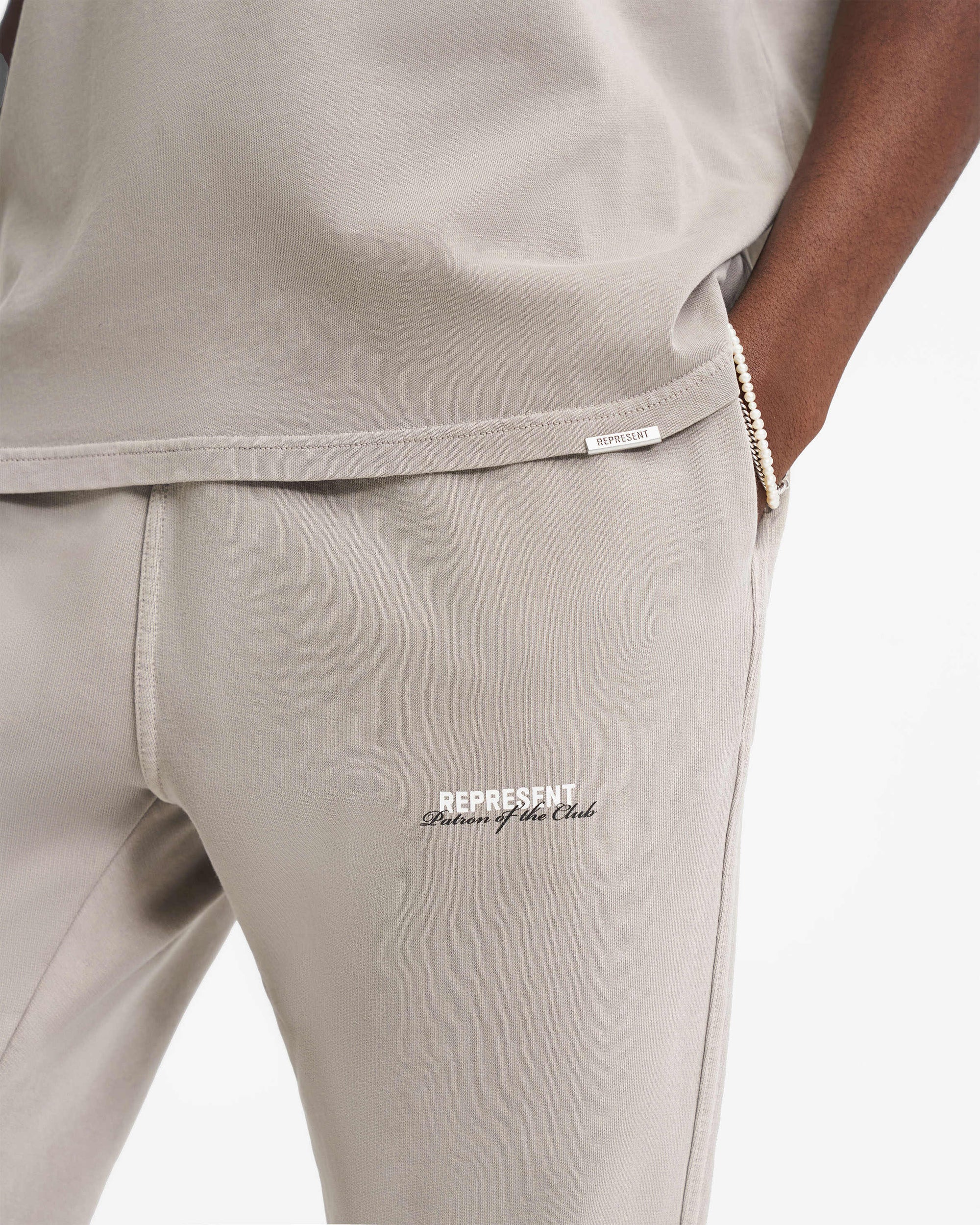 Man wearing mudstone sweatpants on a plain white background | Patron Of The Club Sweatpant in Mudstone | Sweatpants with elasticated waistband and pockets | Patrons Pants | Represent Clo
