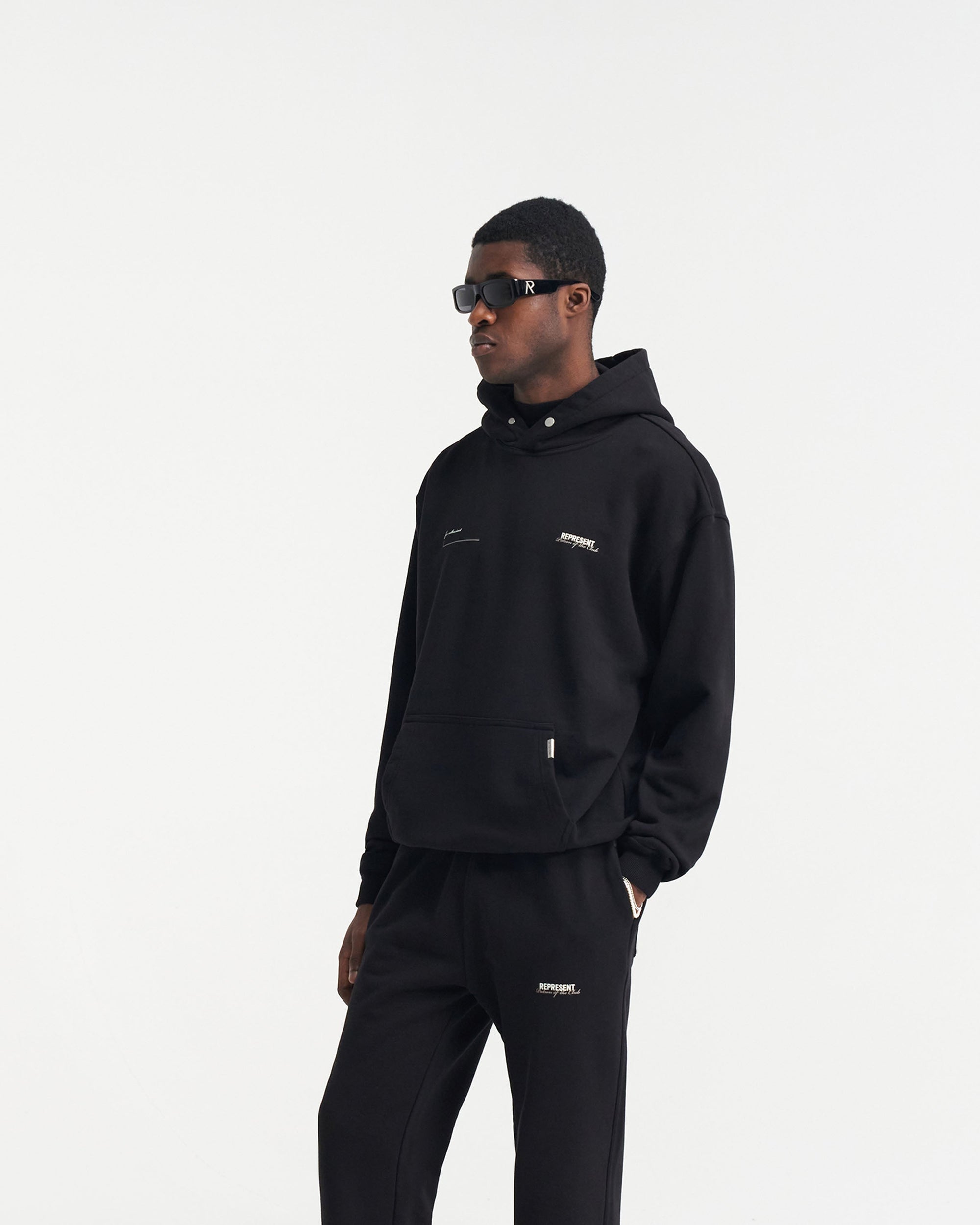 Man wearing a black hoodie on a plain white background | Patron Of The Club Hoodie in Black | Oversized hoodie with Patron of the Club print | Patrons Hoodies | Represent Clo