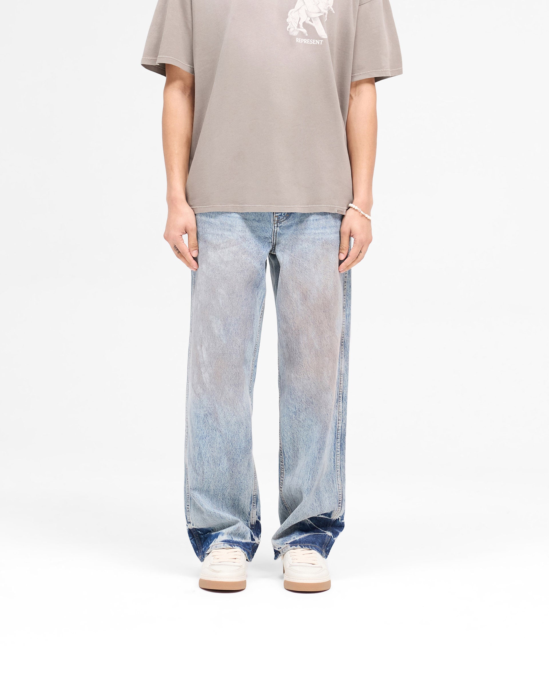 Man wearing mens blue denim jeans on a plain white background | R3 Baggy Denim in Mechanic Blue | Baggy fit jeans with patched dye and signature embroidery | SS25 Denim | Represent Clo
