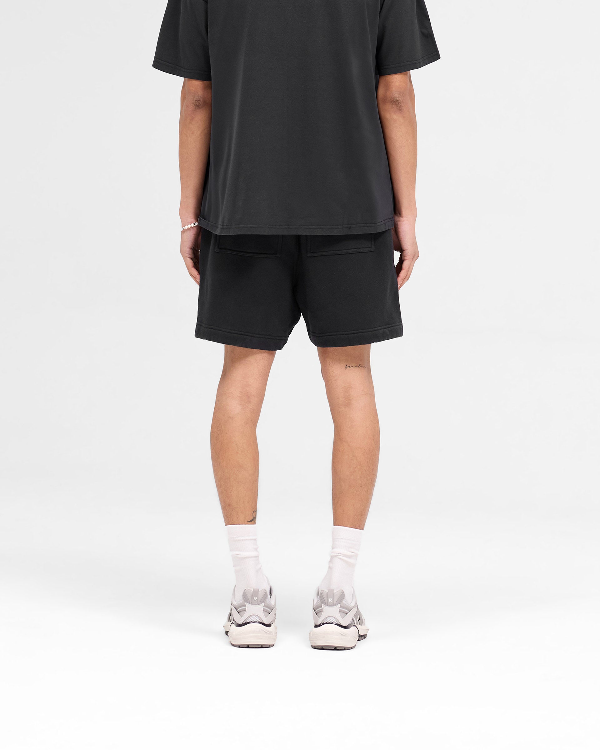 Man wearing black shorts on a plain white background | Rep Applique Shorts in Off Black | Boxy fit shorts with elasticated waistband and applique logo | SS25 Shorts | Represent Clo