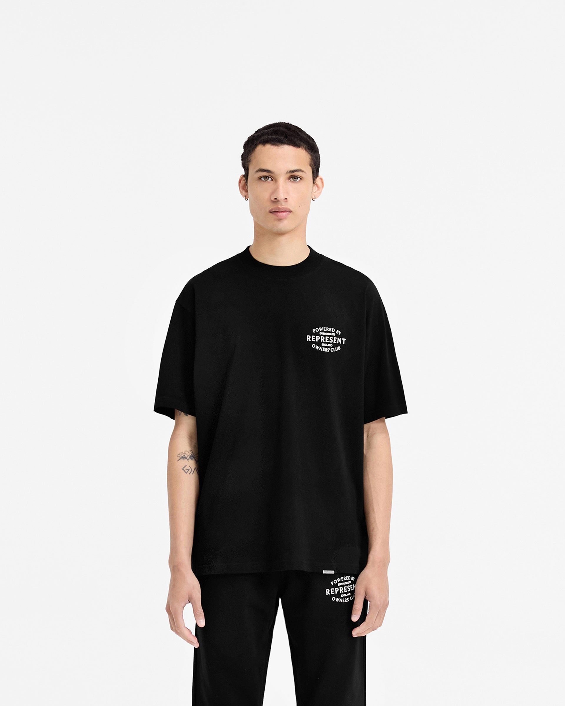 Man wearing a black t-shirt on a plain white background | Represent Owners Club Stamp T-Shirt in Jet Black | Slightly oversized fit t-shirt with metal bar logo | Owners Club T-Shirts | Represent Clo