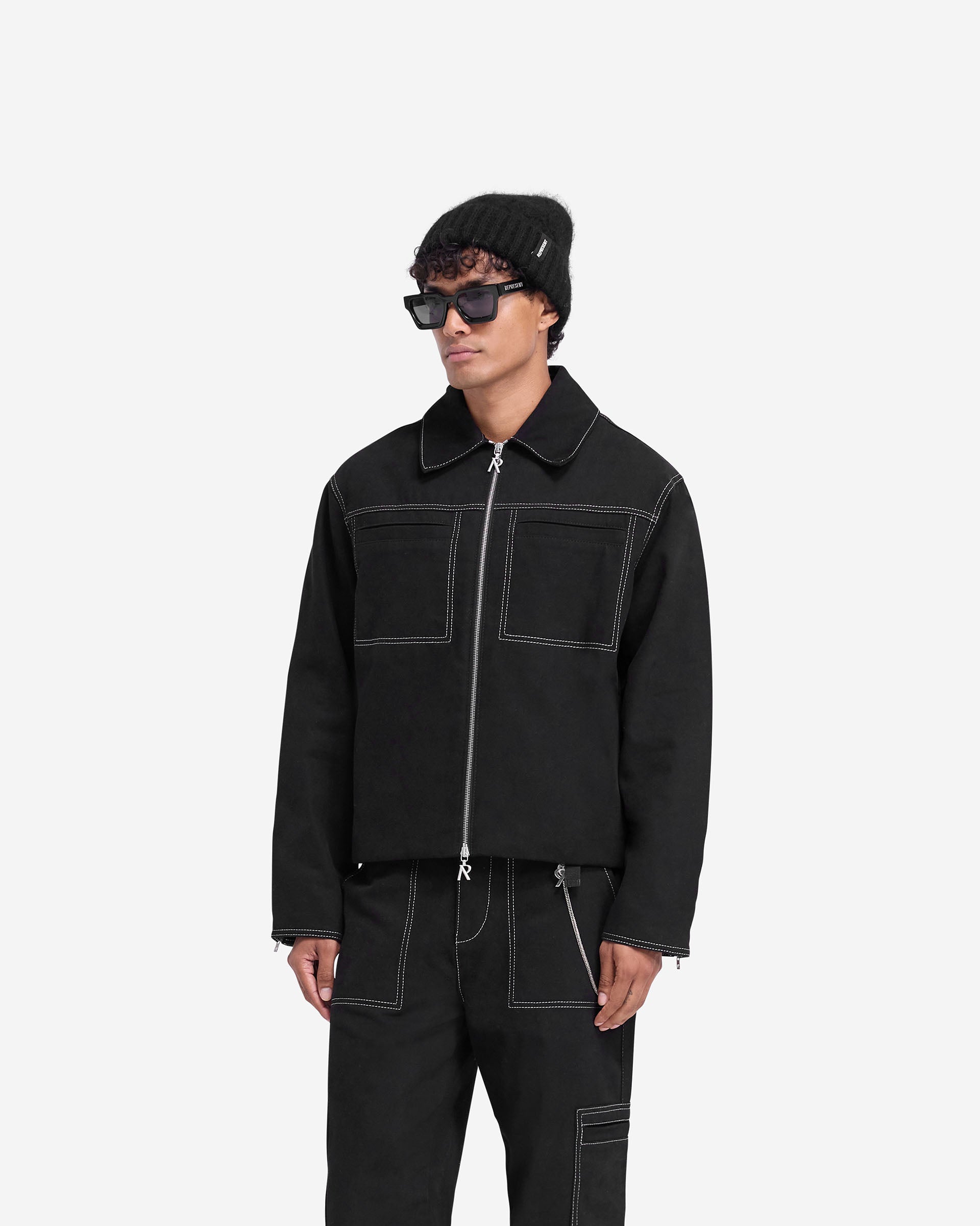 Man wearing a black cotton jacket with contrast stitching on a plain white background | Contrast Stitch Smart Jacket in Jet Black | Oversized smart jacket with double-ended zip | FW24 Outerwear | Represent Clo