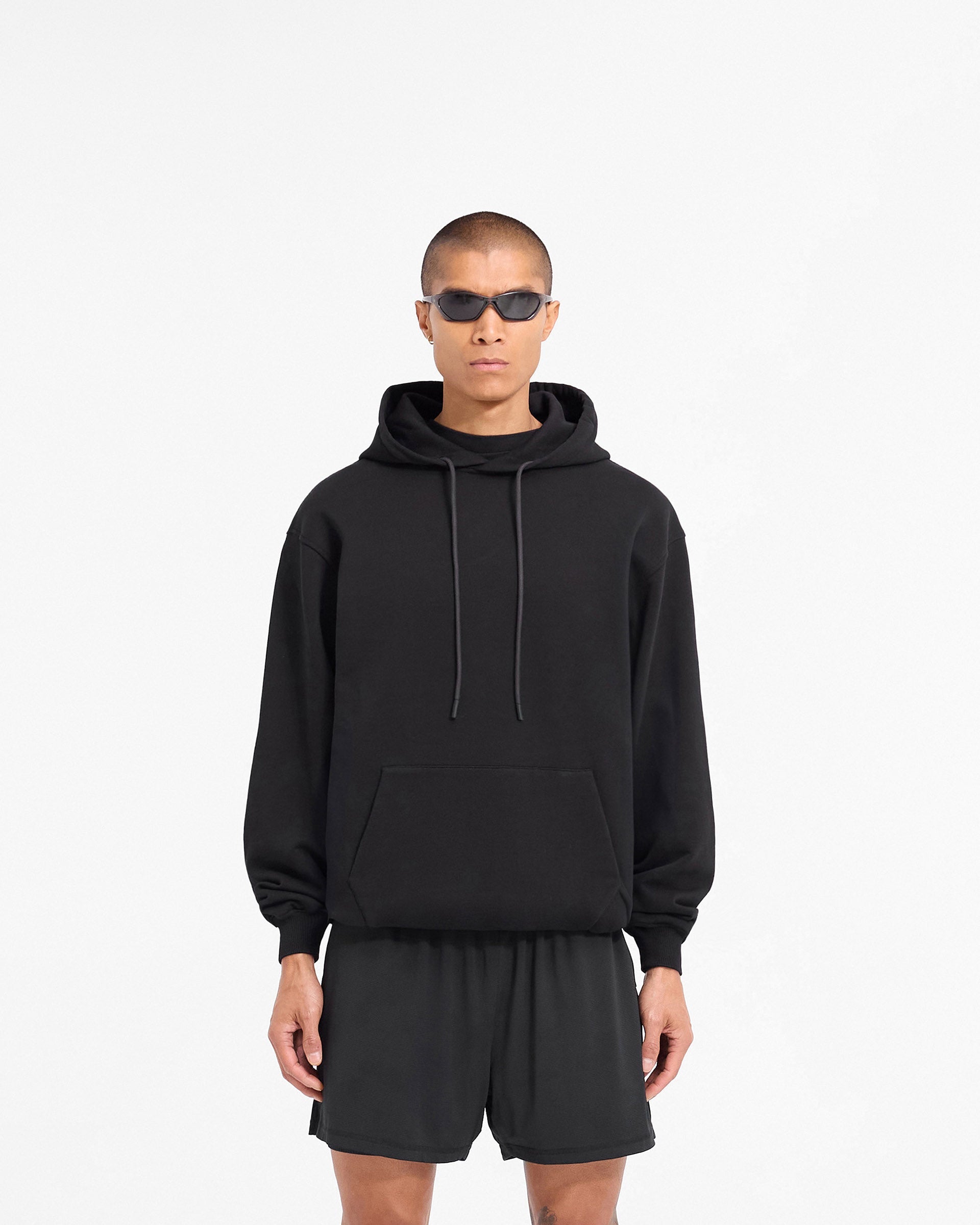 Man wearing a black oversized hoodie on a plain white background | 247 DNA Oversized Hoodie in Black | Oversized hoodie with ribbed cuffs and tonal logo | 247 Hoodies | Represent Clo