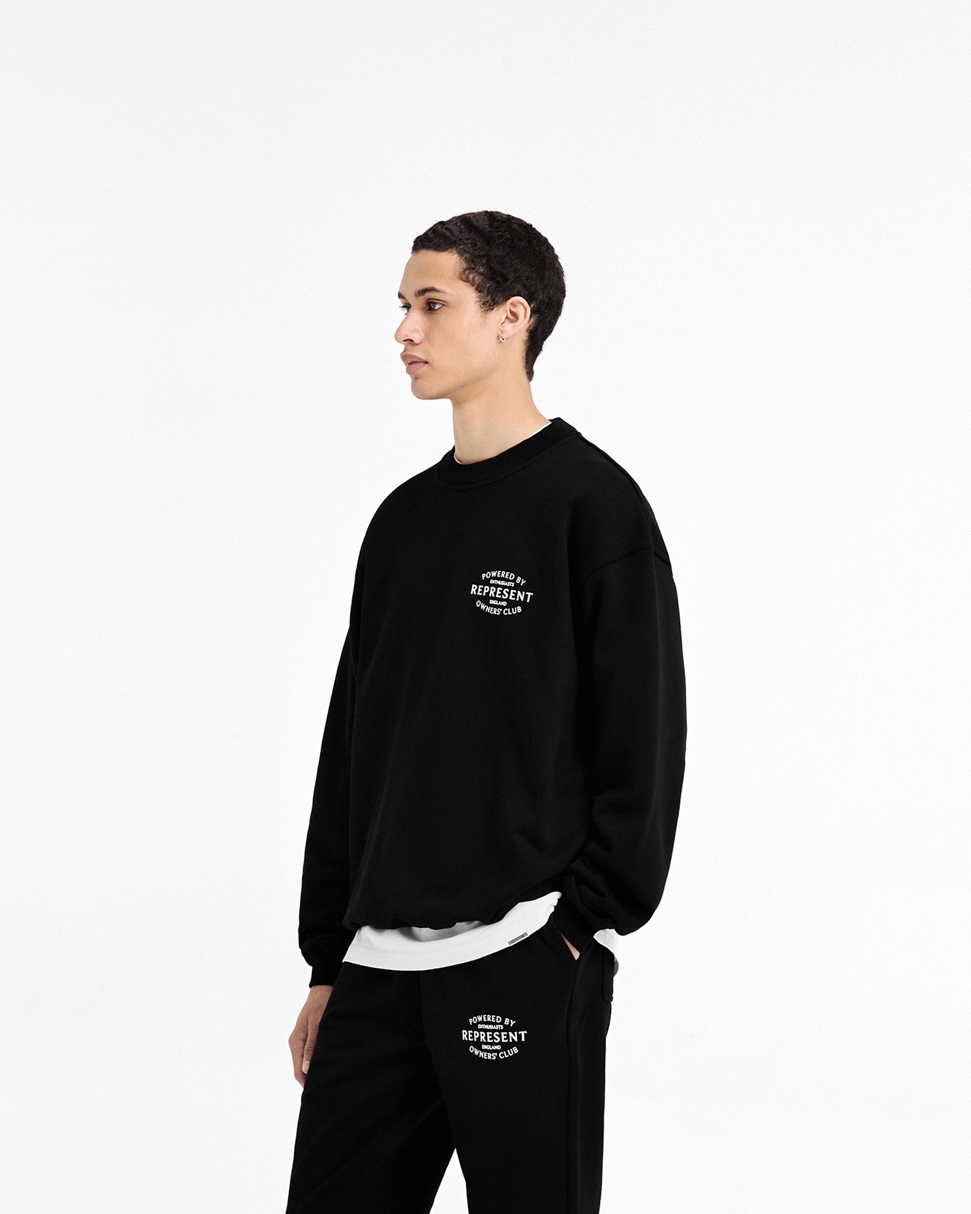 Man wearing a black sweater on a plain white background | Represent Owners Club Stamp Sweater in Jet Black | Oversized fit sweater with high build branding | Owners Club Sweaters | Represent Clo