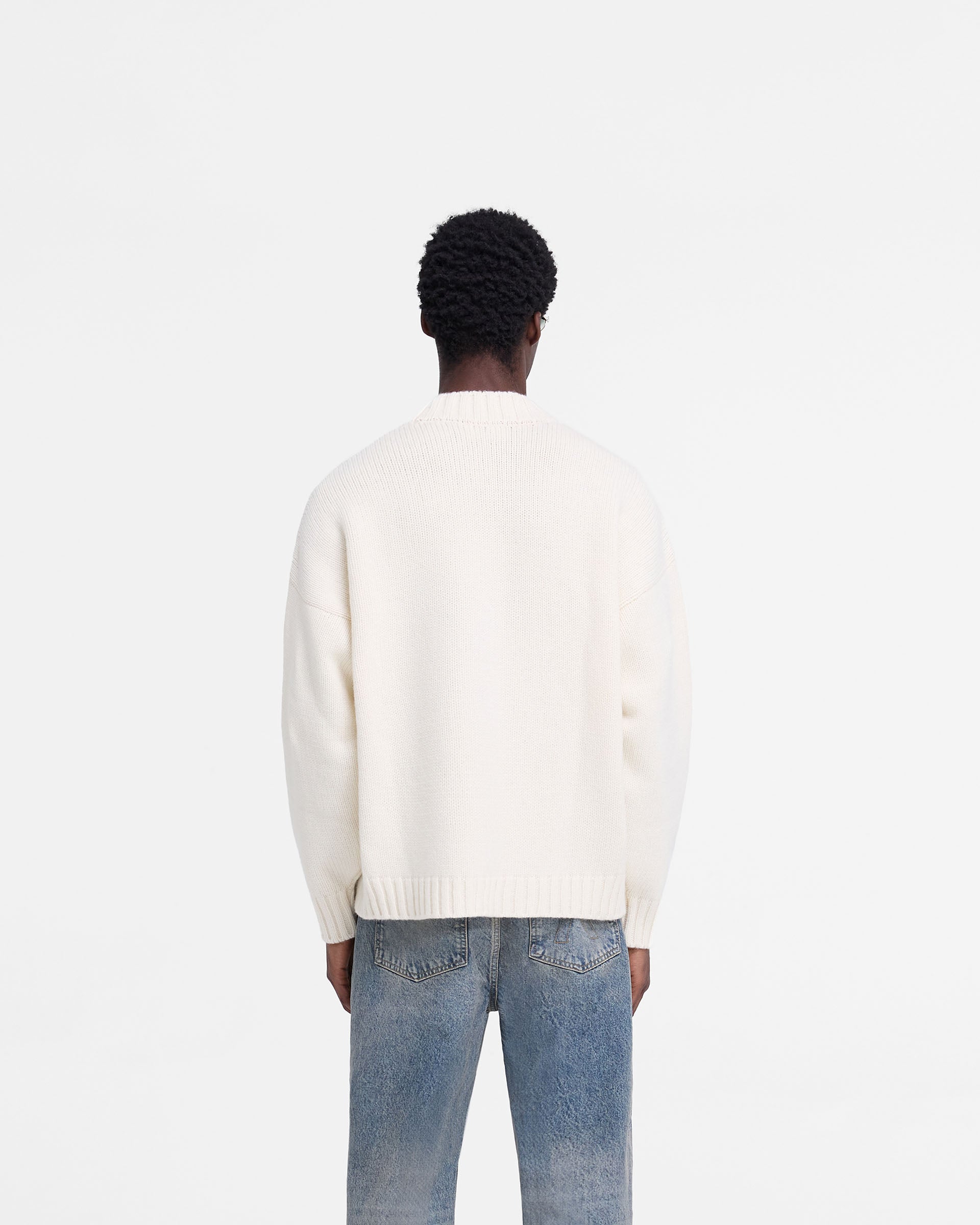Man wearing an oversized oat jumper on a plain white background | Rep Knit Jumper in Oat | Knit jumper with ribbed cuffs and distressed branding | FW24 Knitwear | Represent Clo