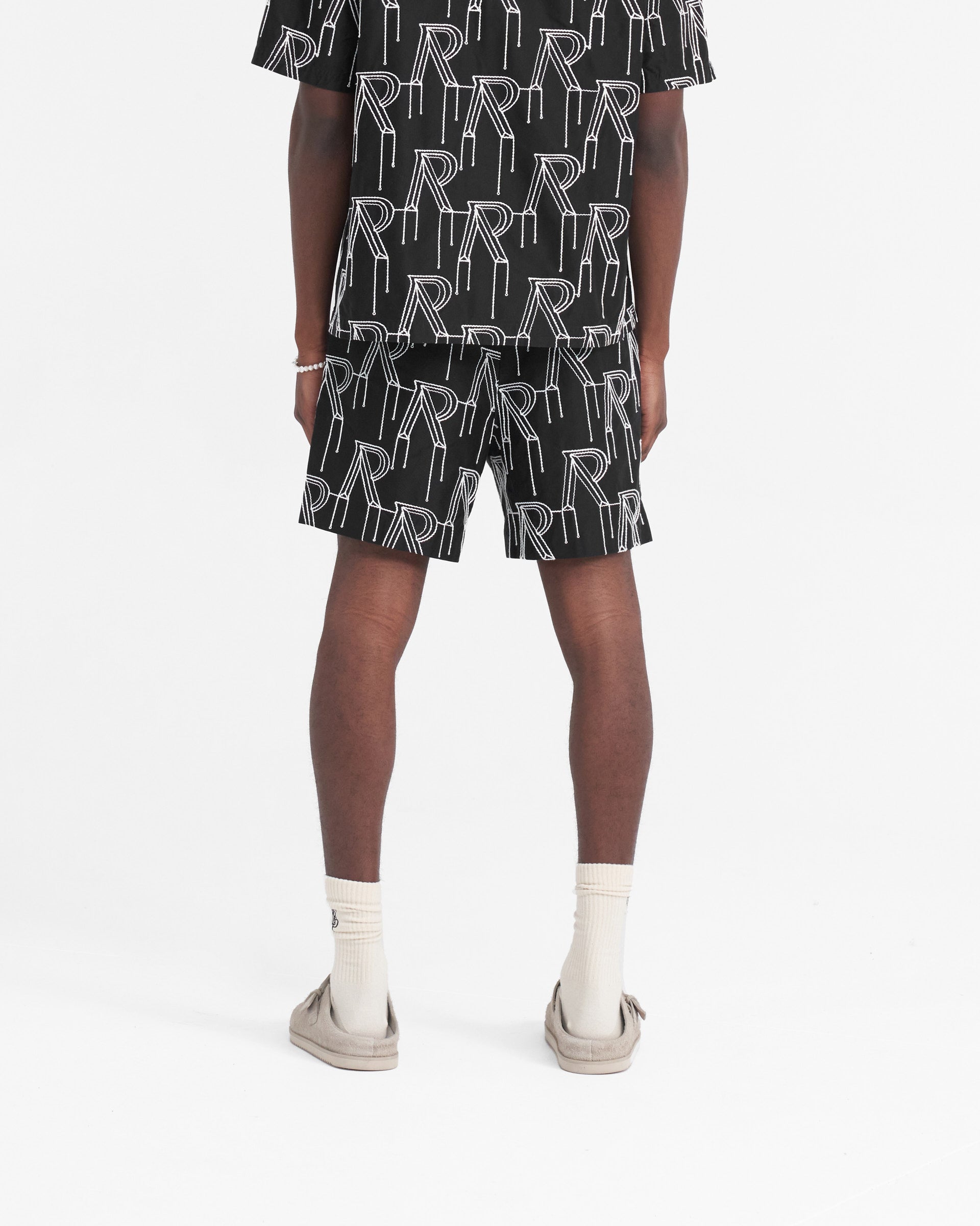 Man wearing black tailored shorts on a plain white background | Embroidered Initial Tailored Short in Black | Tailored shorts with embroidered initial logos | SS24 Shorts | Represent Clo