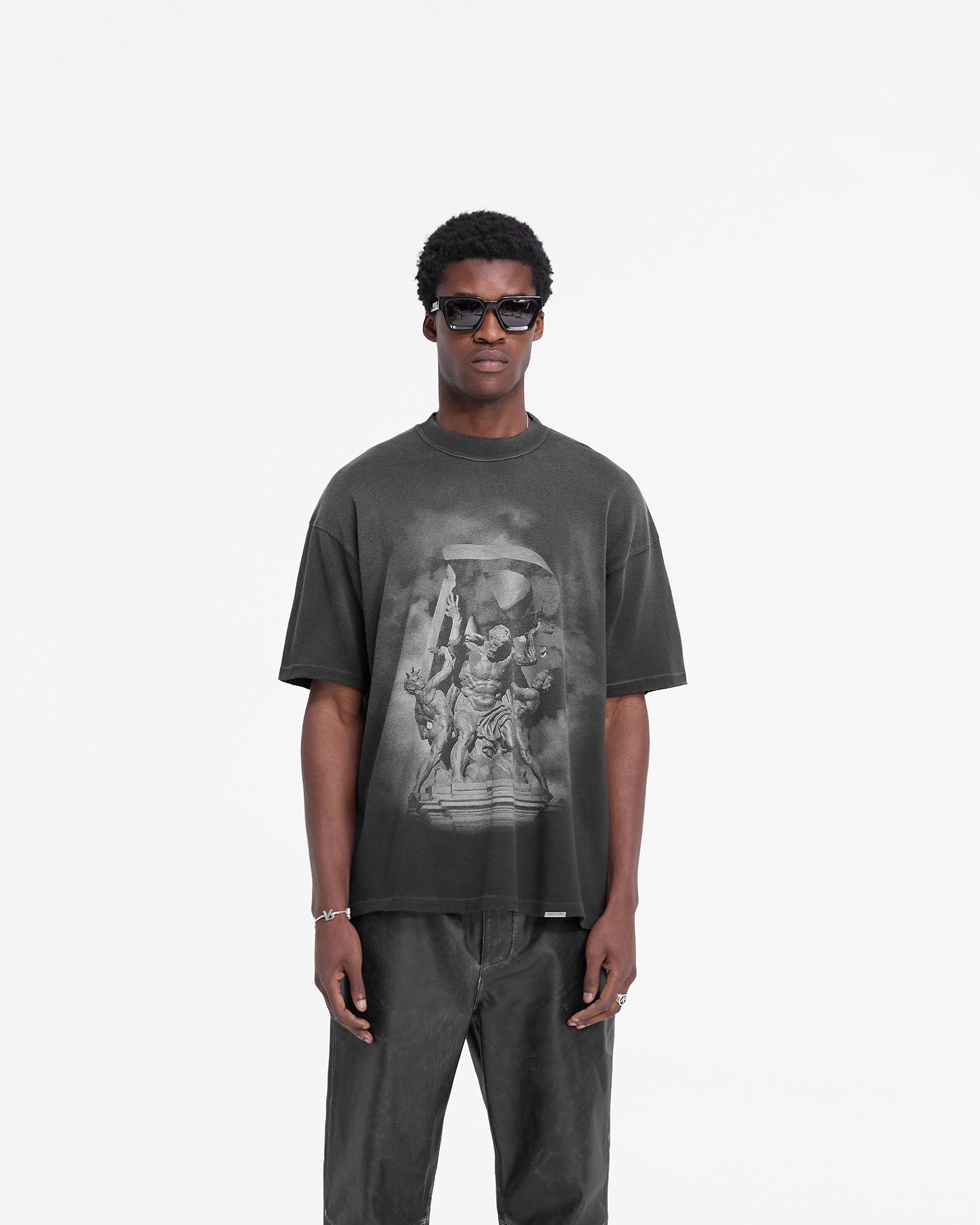 Man wearing a black t-shirt with distressed details on a plain white background | Atlas T-Shirt in Stained Black | Slightly oversized t-shirt with puff print graphics | FW24 T-Shirts | Represent Clo