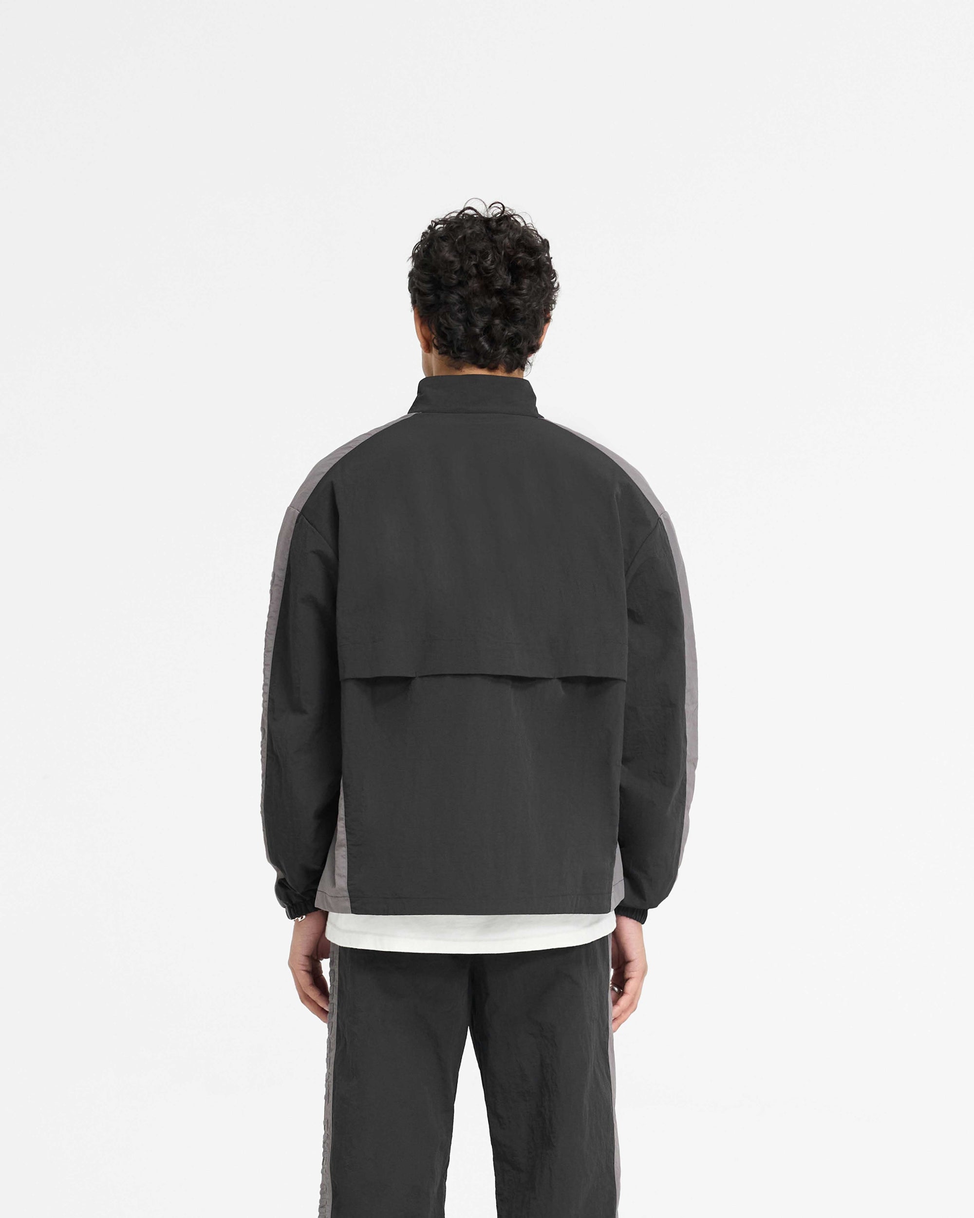 Man wearing a black nylon track jacket on a plain white background | Nylon Track Jacket in Black | Slightly oversized track jacket with storm flaps and zip pockets | PRE SS25 Outerwear | Represent Clo