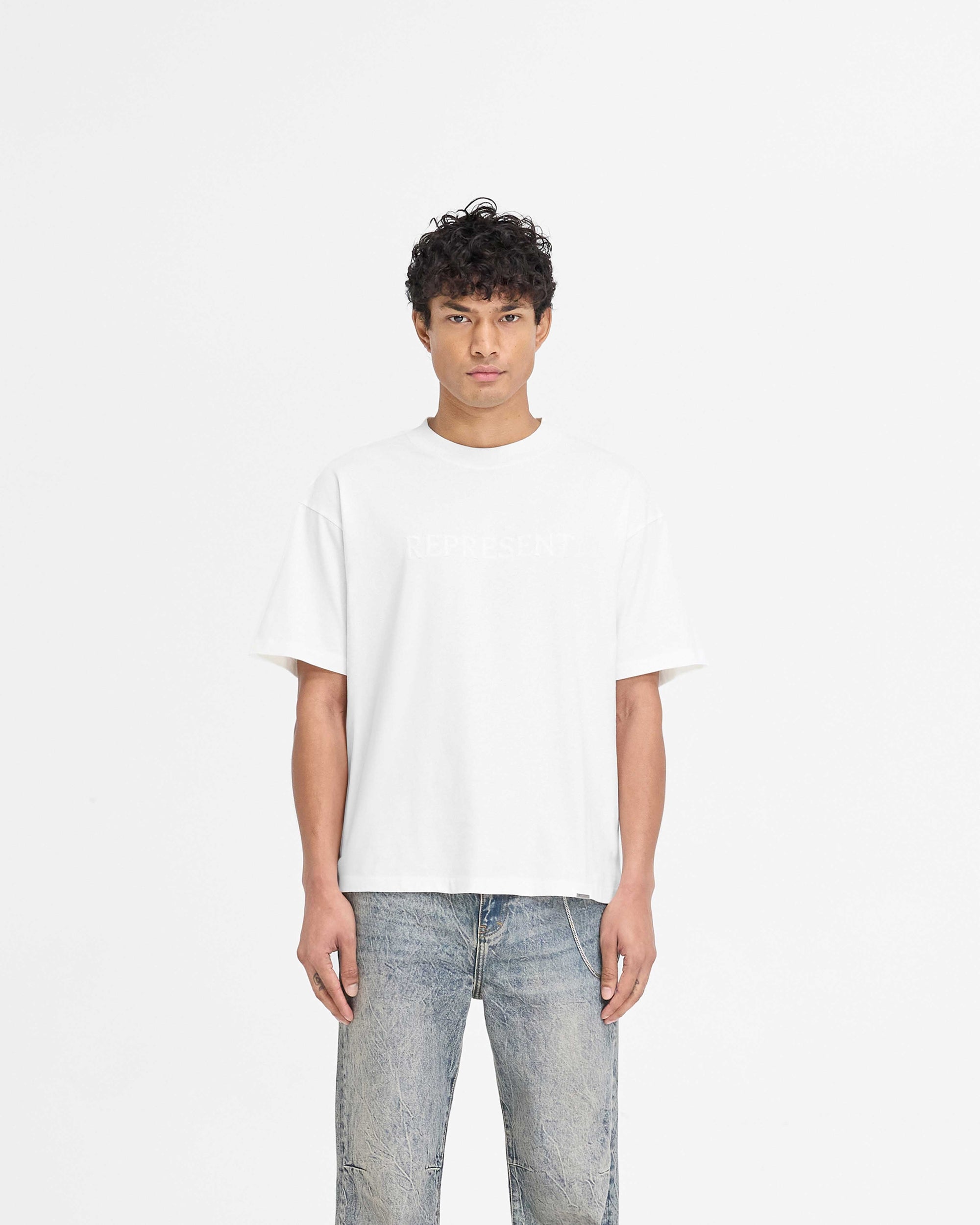 Man wearing a white t-shirt on a plain white background | Serif Logo T-Shirt in Flat White | Slightly oversized t-shirt with high build embroidered branding | PRE SS25 T-Shirts | Represent Clo