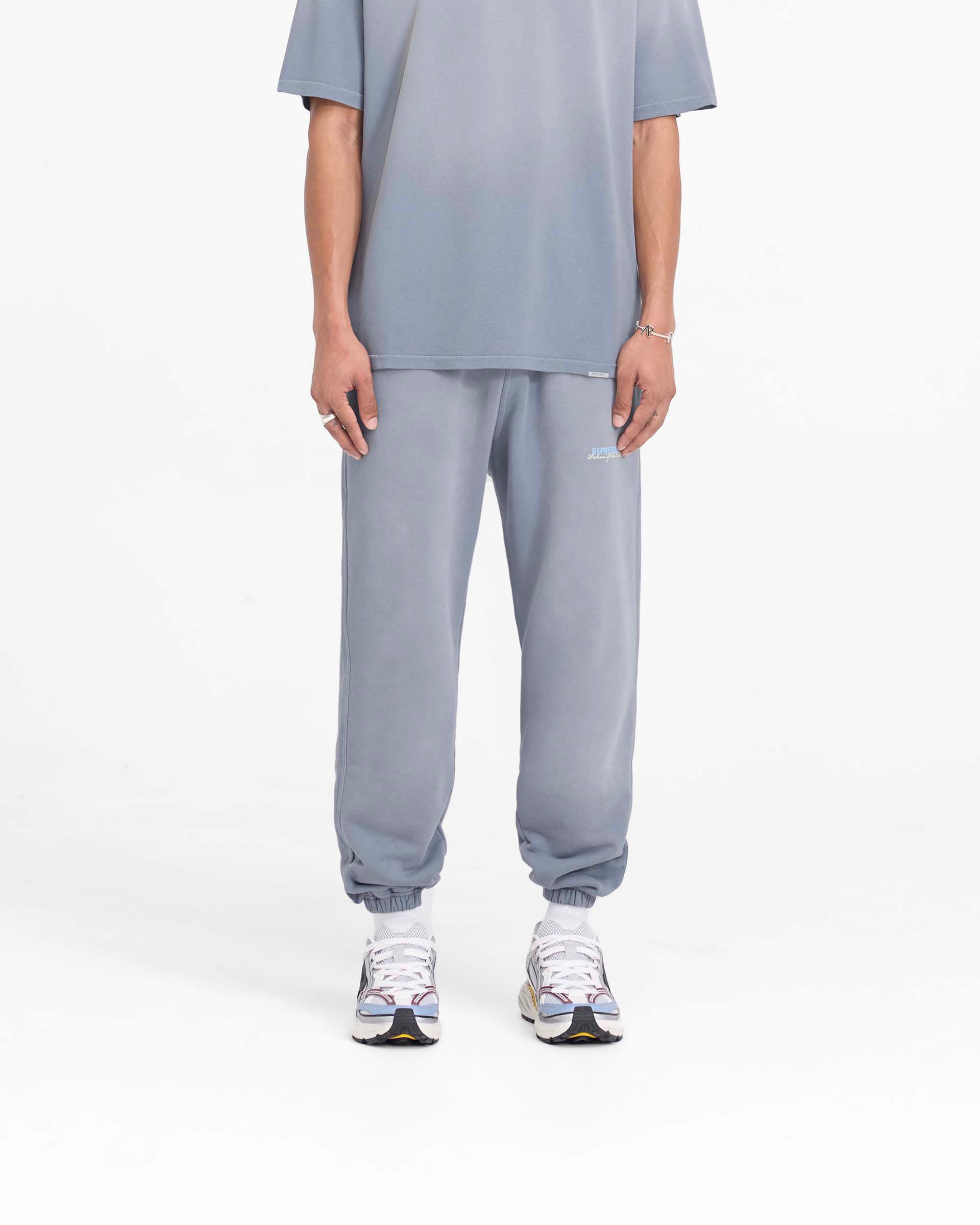 Man wearing grey sweatpants on a plain white background | Patron Of The Club Sweatpant in Washed Grey | Heavyweight cotton sweatpants with elasticated waistband | Patrons Pants | Represent Clo