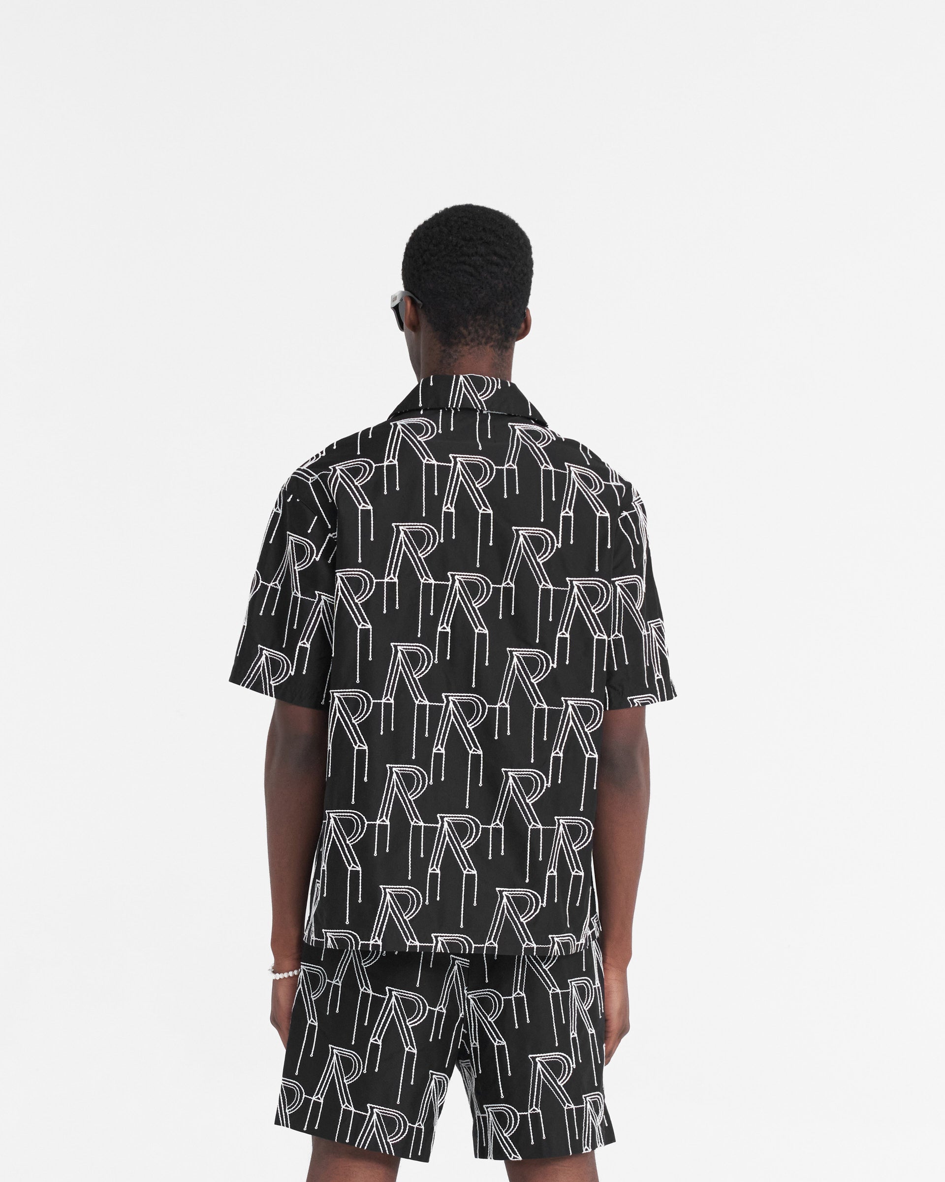 Man wearing a black short-sleeved shirt on a plain white background | Embroidered Initial Overshirt in Black | Oversized shirt with chain stitch embroidery and revere collar | SS24 Shirts | Represent Clo