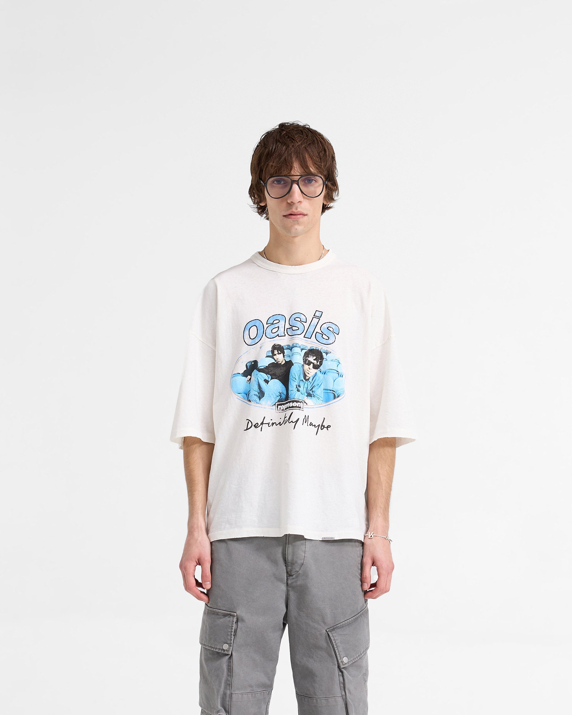 Man wearing a white t-shirt with graphics on a plain white background | Represent X Oasis Maine Road T-Shirt in Flat White | Oversized boxy t-shirt with distressed Oasis imagery | FW24 T-Shirts | Represent Clo