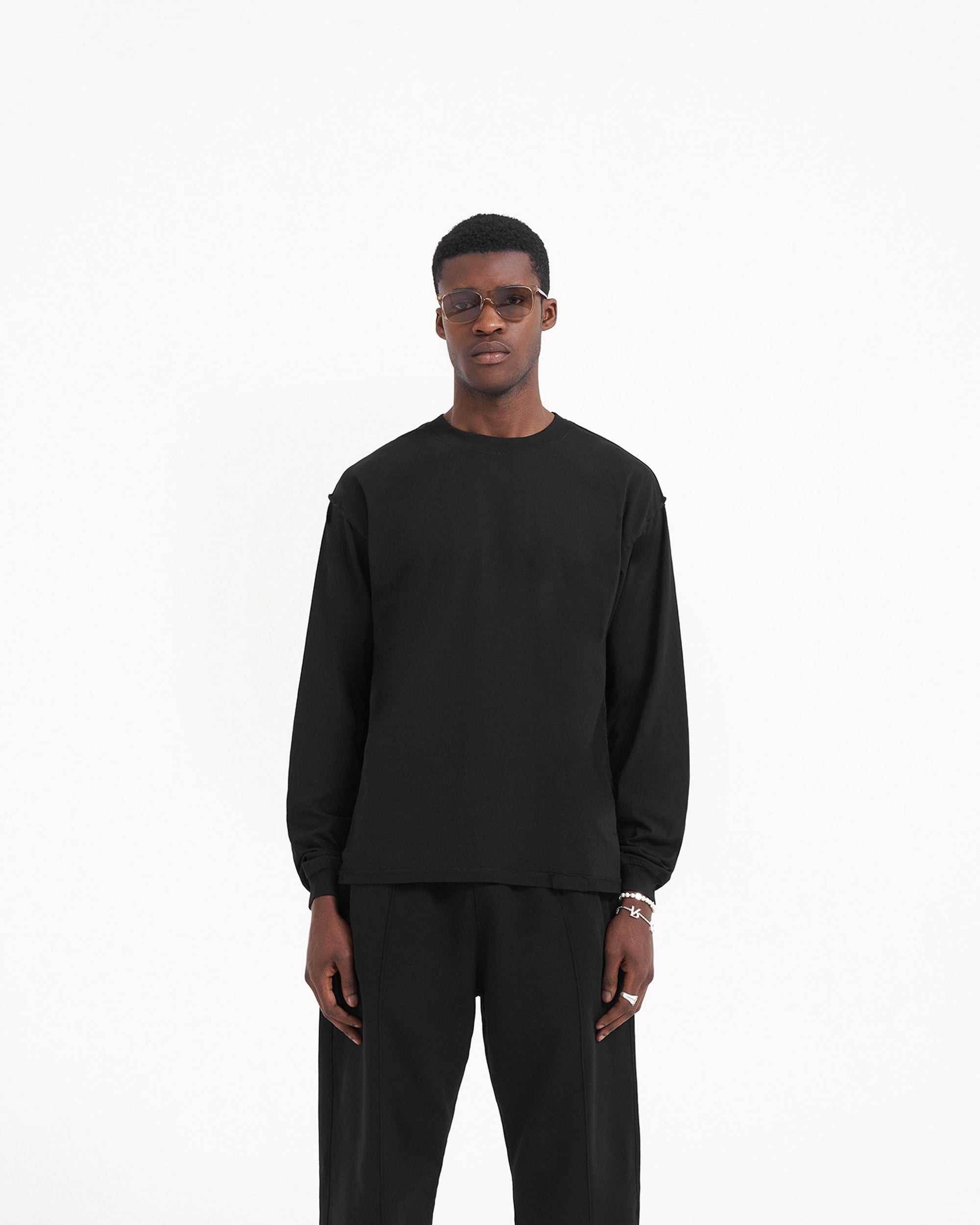 Man wearing a black long sleeve t-shirt on a plain white background | Initial Long Sleeve T-Shirt in Jet Black | Slightly oversized t-shirt with external overlock seams | Initial T-Shirts | Represent Clo