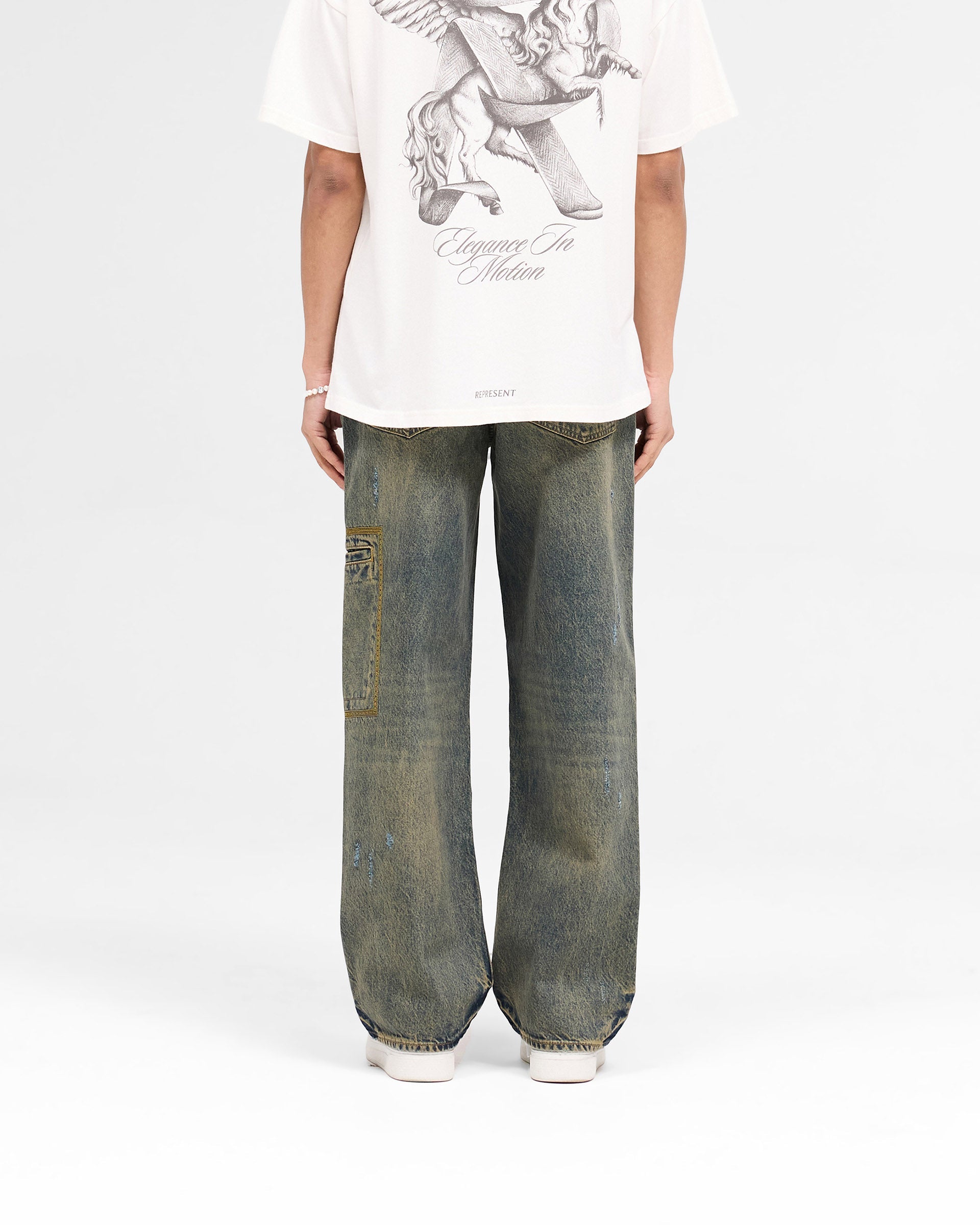 Man wearing baggy fit blue jeans on a plain white background | R3 Drive Denim in Tobacco Blue | Distressed denim with utilitarian design | SS25 Denim | Represent Clo