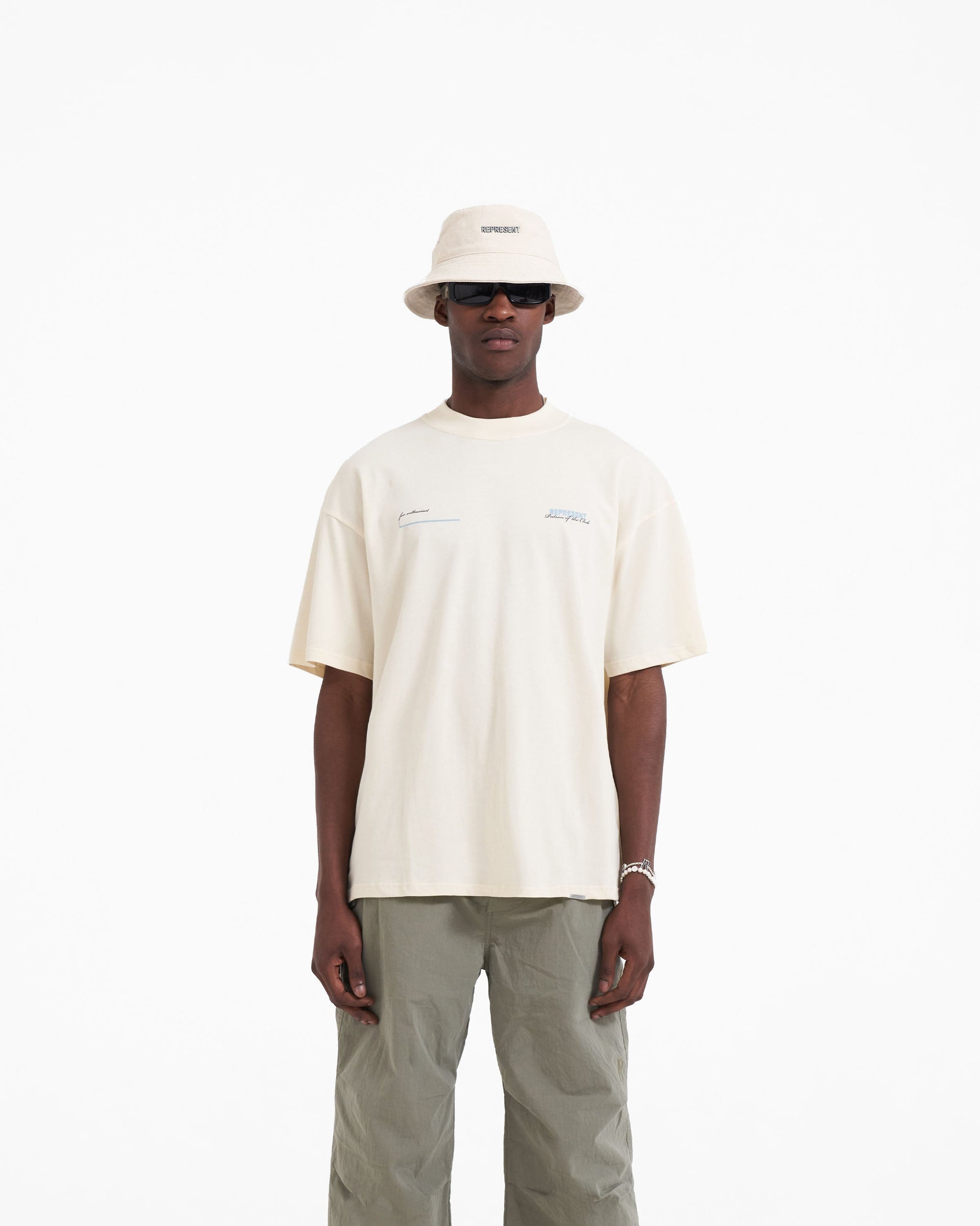Man wearing a buttercream t-shirt on a plain white background | Patron Of The Club T-Shirt in Buttercream Powder Blue | Slightly oversized medium weight jersey cotton t-shirt | Patrons T-Shirts | Represent Clo