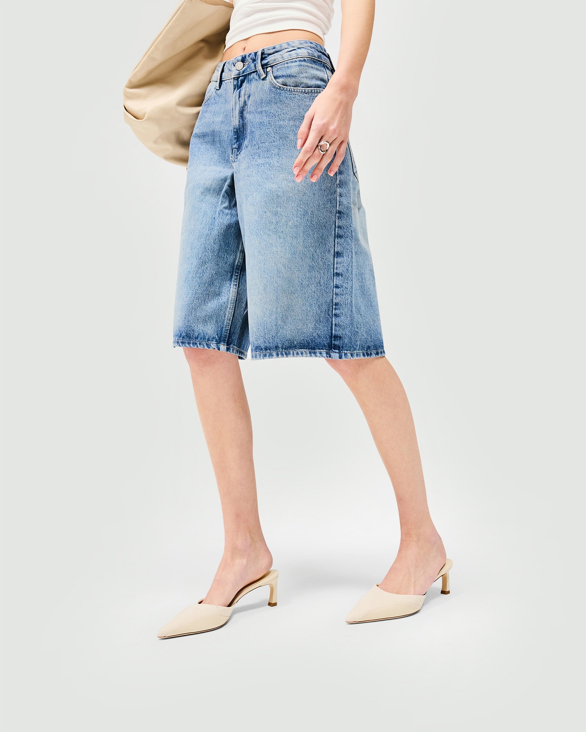 Woman wearing washed blue denim shorts on a plain white background | Denim Bermuda Short in Washed Blue | Classic flattering fit denim shorts | Womens SS25 Denim | Represent Clo