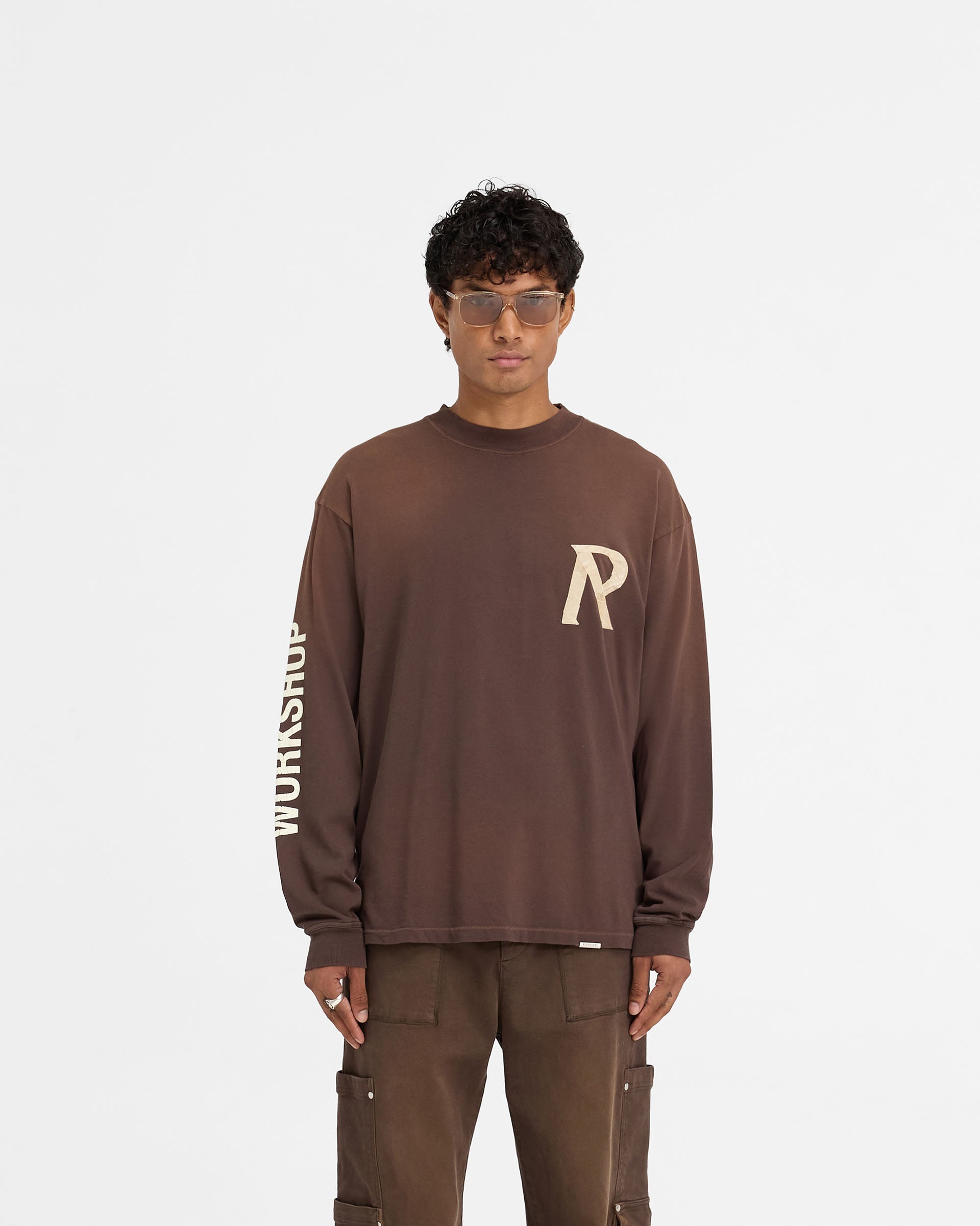 Man wearing a cedar long sleeve t-shirt on a plain white background | Masking Tape Initial Long Sleeve T-Shirt in Cedar | Oversized t-shirt with 3D masking tape effect | FW24 T-Shirts | Represent Clo