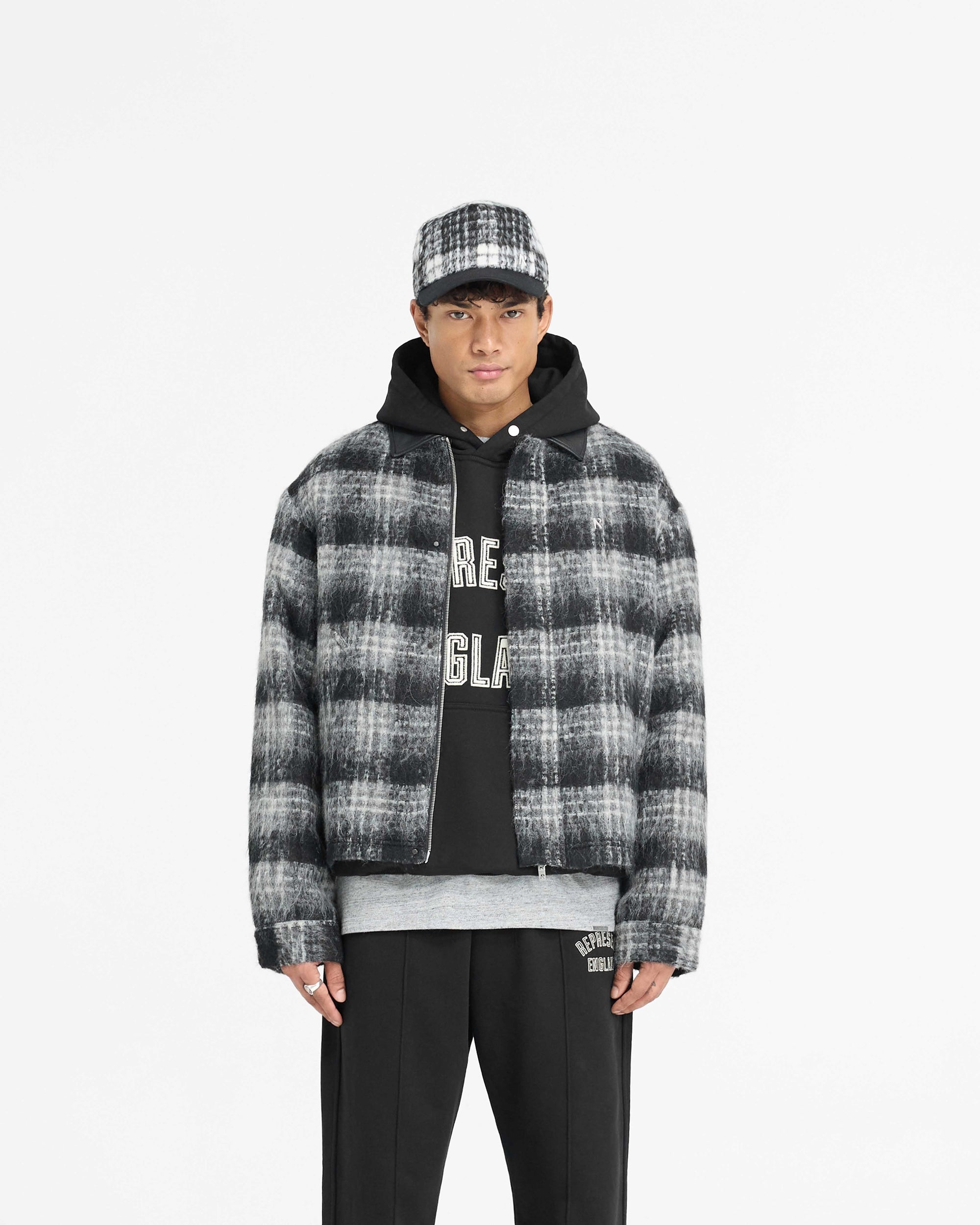 Man wearing a black check flannel overshirt on a plain white background | Flannel Check Overshirt in Jet Black | Oversized boxy shirt with cropped body and jacquard lining | PRE SS25 Shirts | Represent Clo