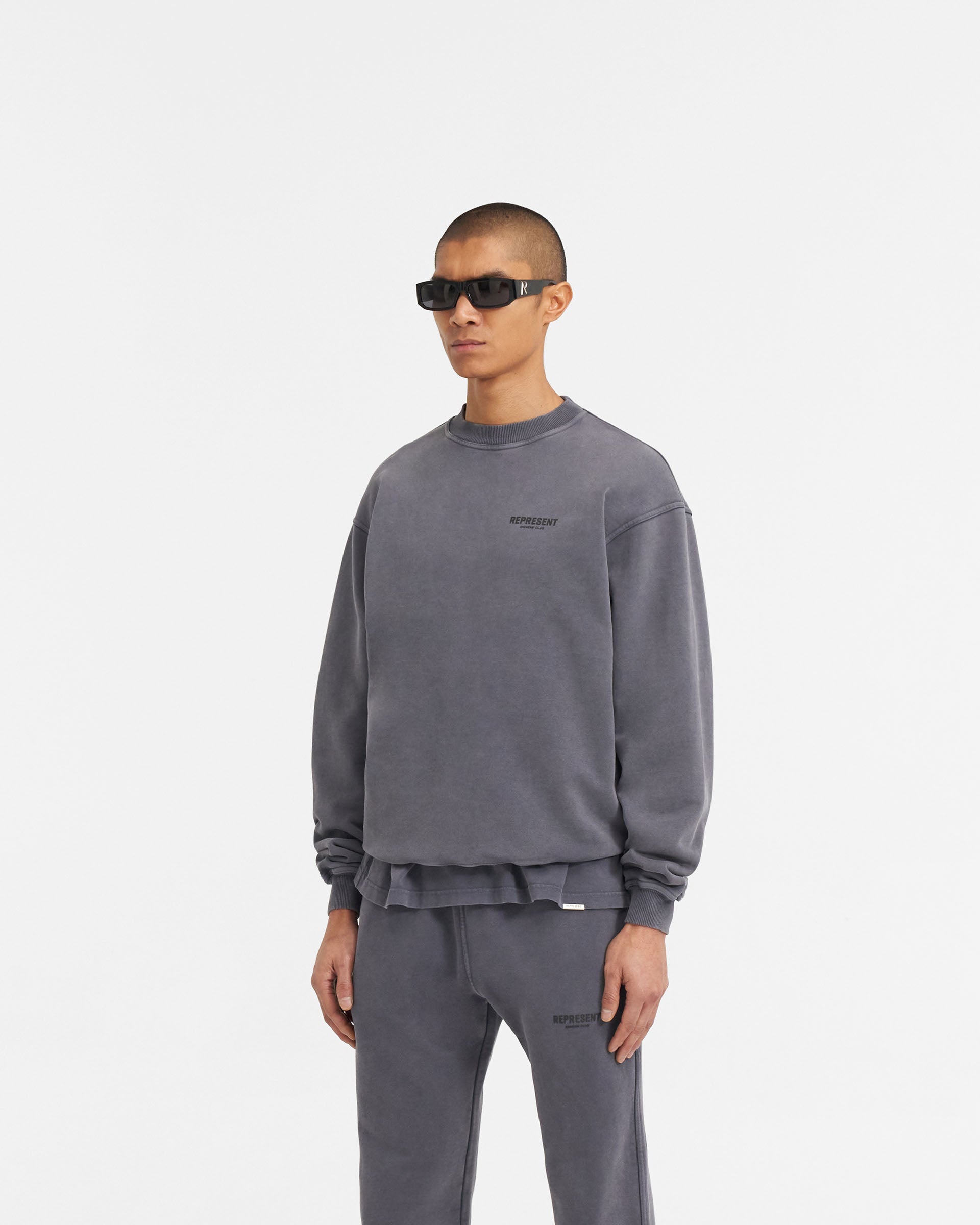 Man wearing a grey oversized sweater on a plain white background | Represent Owners Club Sweater in Storm | Heavyweight jersey cotton crewneck sweater with high build branding | Owners Club Sweaters | Represent Clo