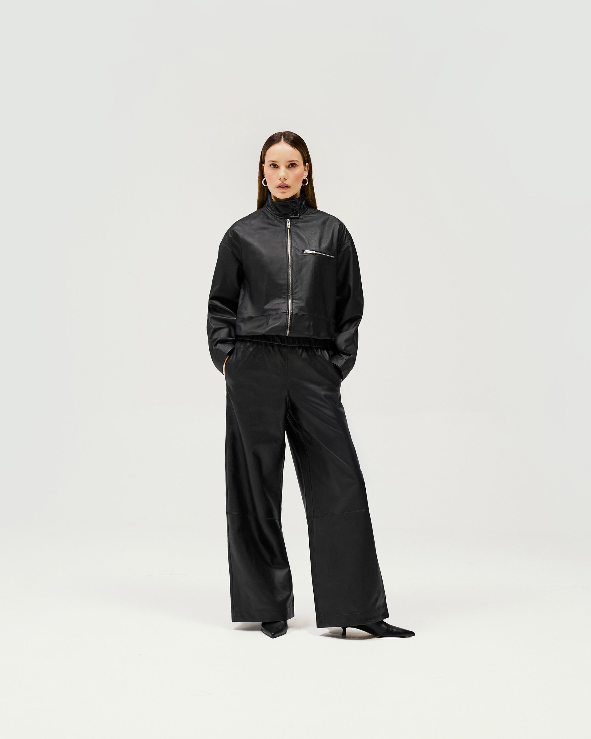Woman wearing black track pants on a plain white background | Fuel Trouser in Jet Black | Lamb leather track pant with relaxed fit and wide leg | Womens SS25 Bottoms | Represent Clo