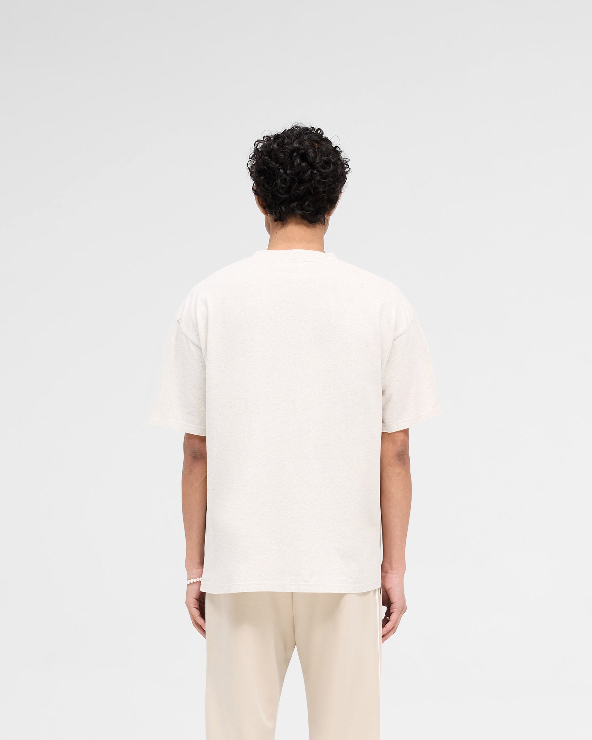 Man wearing a cream t-shirt on a plain white background | Rep Applique T-Shirt in Cream Marl | Slightly oversized t-shirt with textured applique | SS25 T-Shirts | Represent Clo
