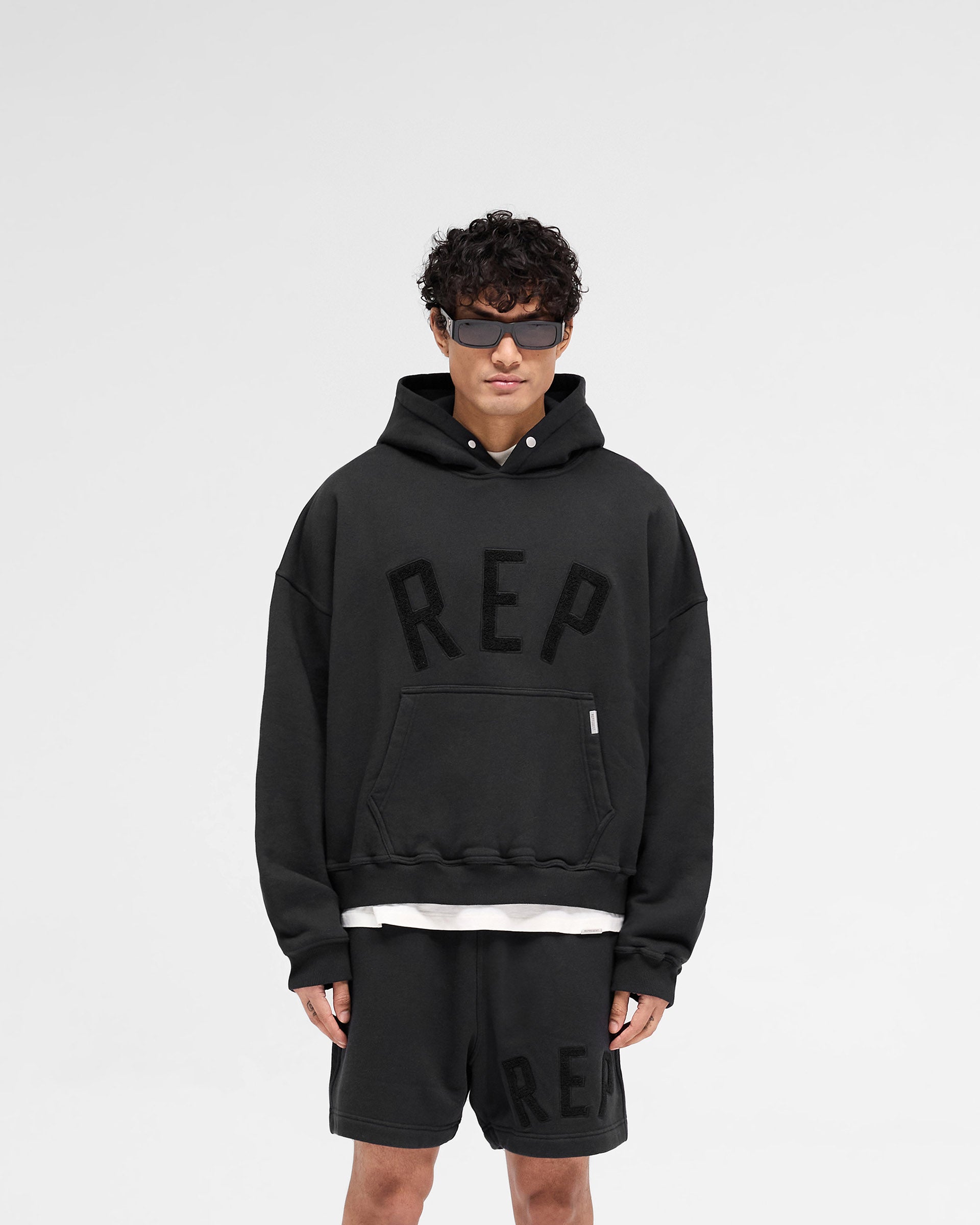 Man wearing an off black hoodie on a plain white background | Rep Applique Hoodie in Off Black | Boxy fit cotton hoodie with textured applique | SS25 Hoodies | Represent Clo